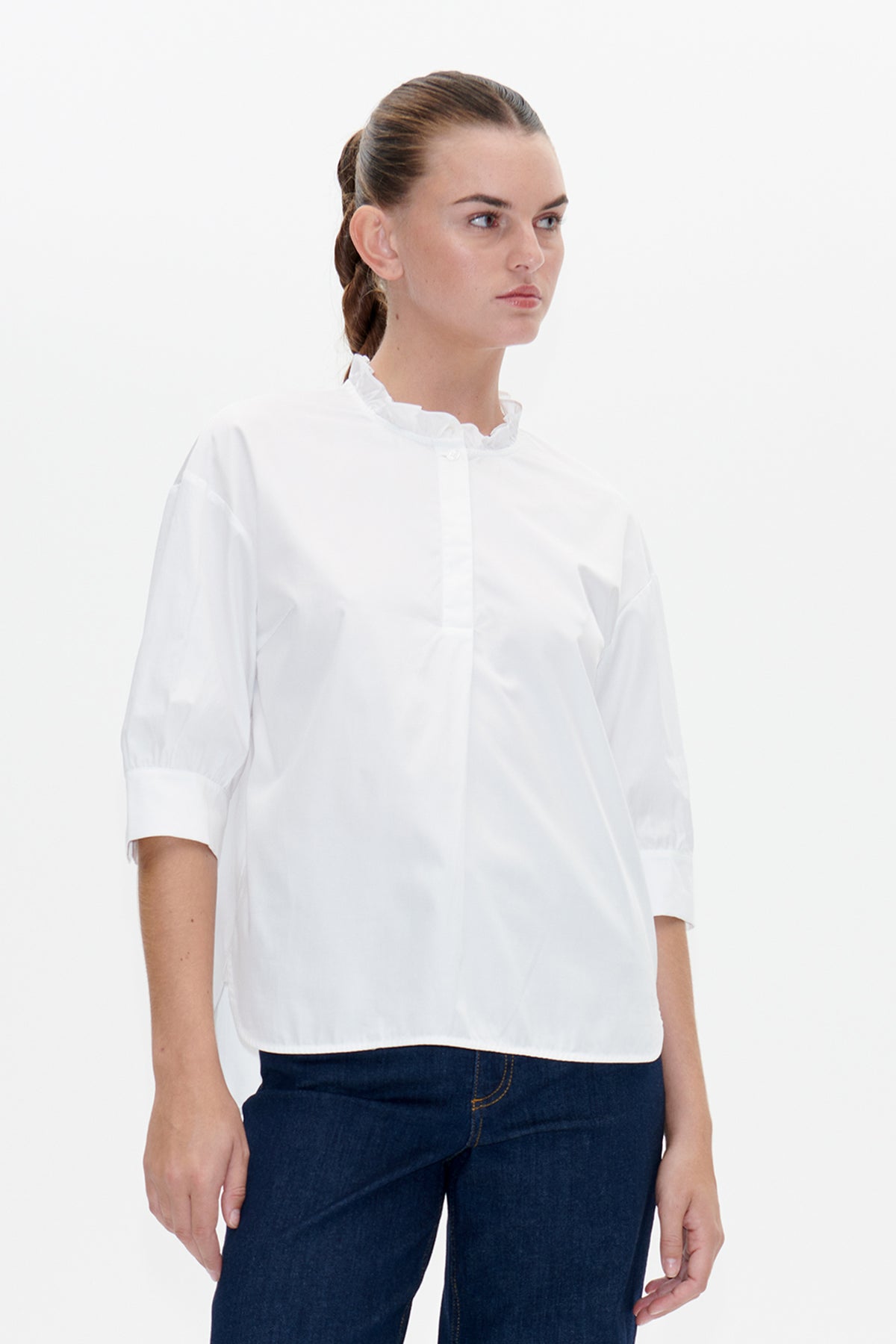 Vorderansicht einer weißen Bluse mit Rüschen-Stehkragen, Knopfleiste und kurzen gerafften Ärmeln, kombiniert mit dunkelblauer Jeans.
