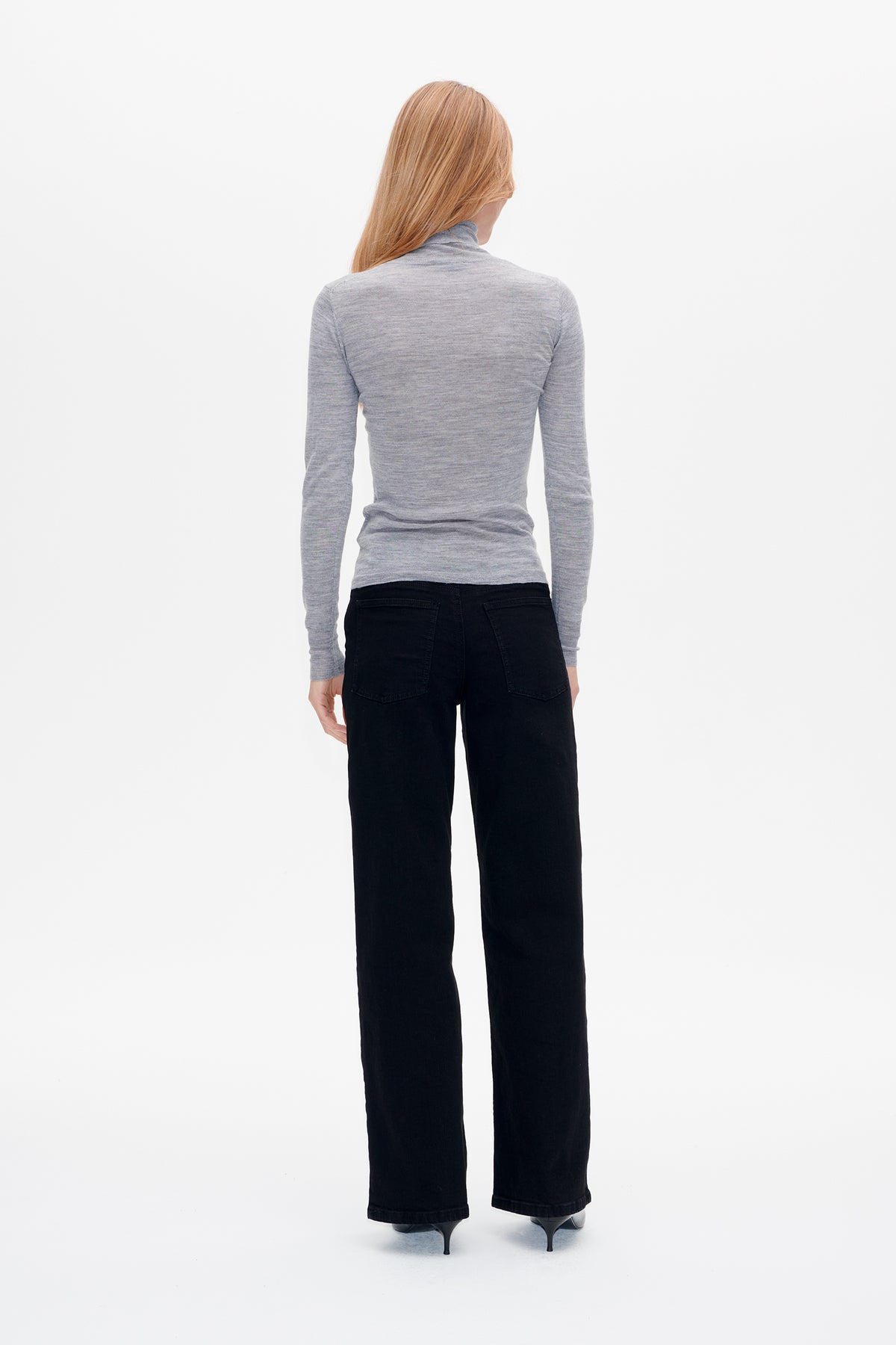 Back view of a heather grey, long-sleeved high-neck top styled with black wide-leg trousers.