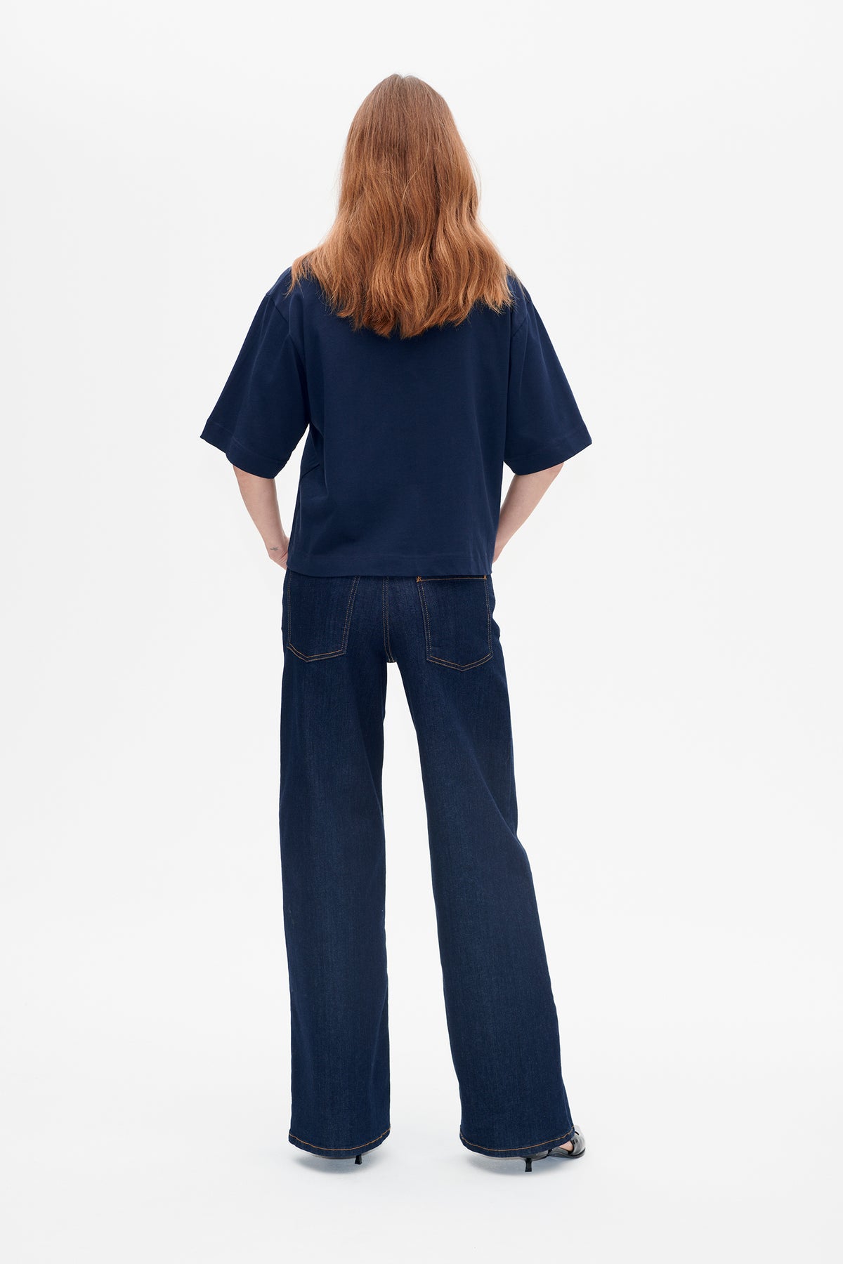 Back view of a model wearing a plain navy short-sleeved T-shirt and dark indigo wide-leg jeans with contrast stitching and back pockets.