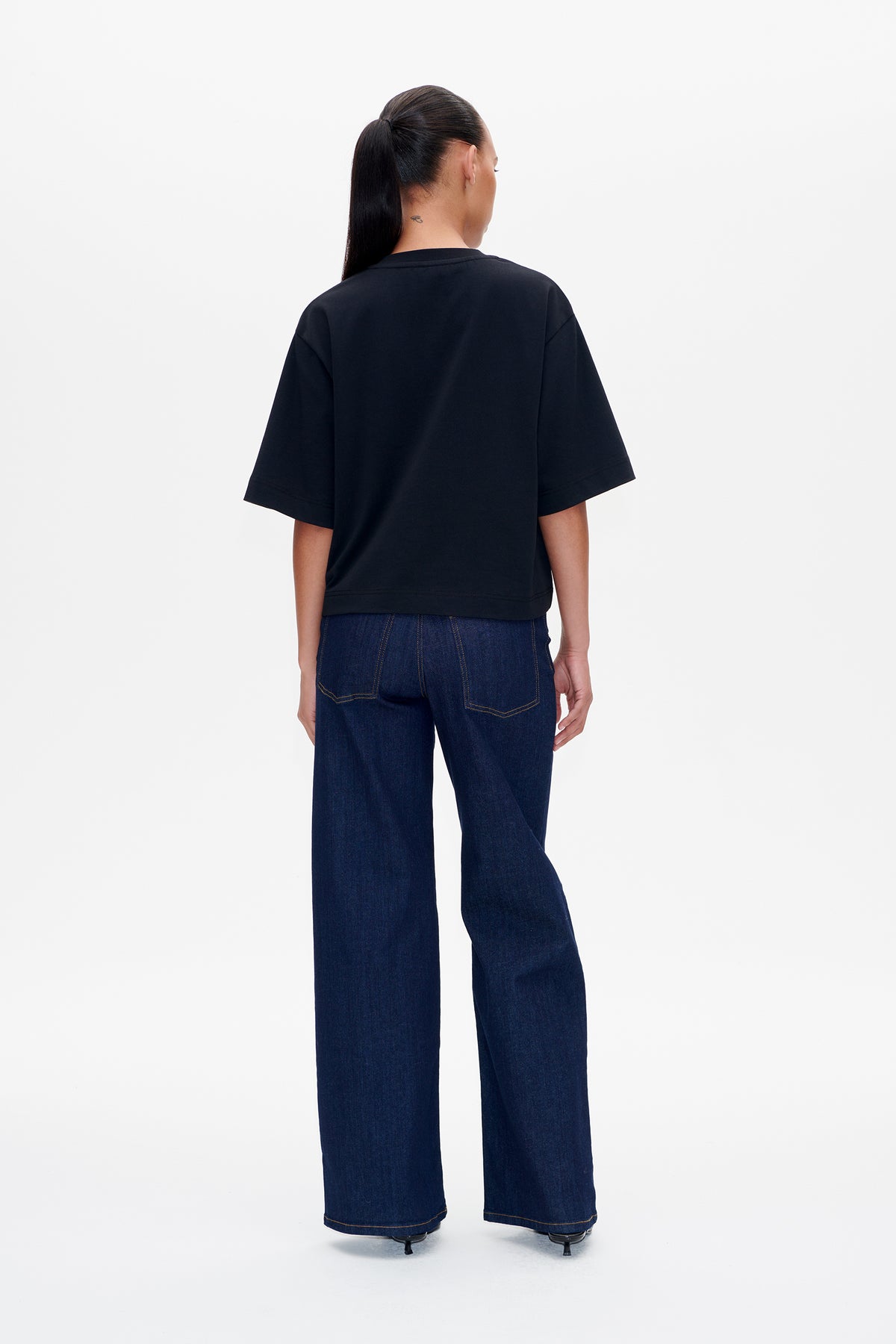 Back view of a model wearing a plain black short-sleeved T-shirt with dark blue wide-leg jeans.