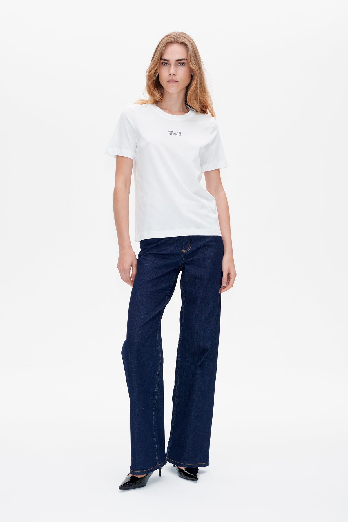 Vue de face d'un t-shirt blanc à manches courtes avec petit lettrage sur la poitrine, porté avec un jean large bleu foncé.