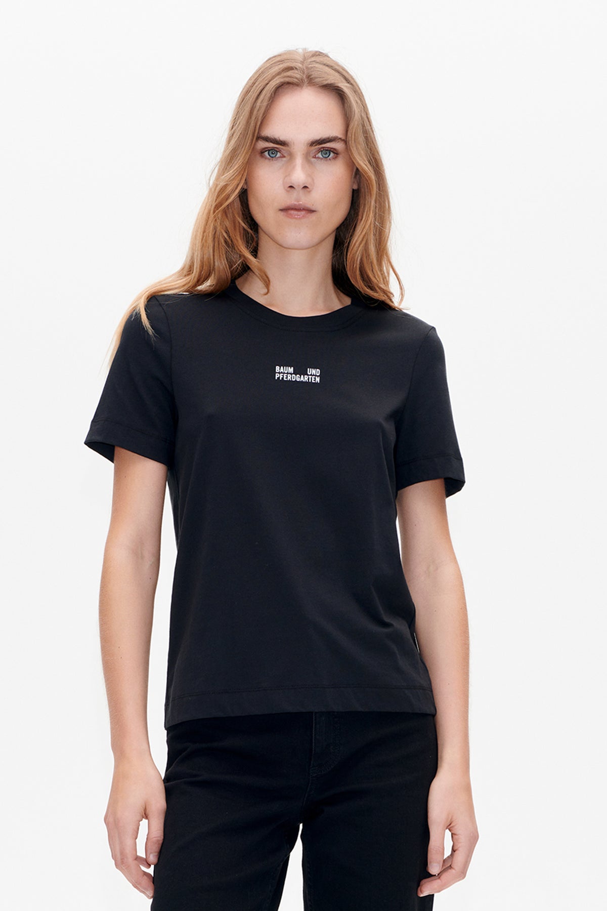 Vue de face d'un t-shirt noir à manches courtes et à col rond, avec un petit logo blanc Baum und Pferdgarten sur la poitrine.