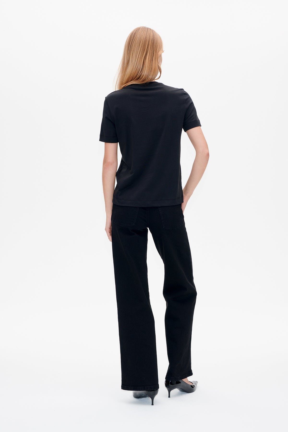 Vue de dos d'un t-shirt noir uni à manches courtes porté avec des jeans larges noirs.