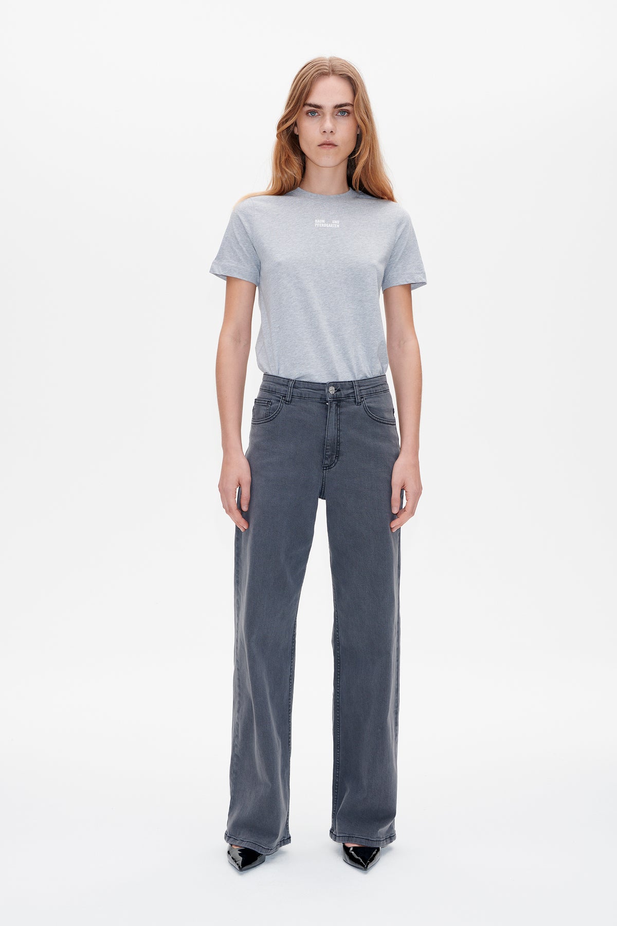 Front view of a model wearing a light grey T-shirt with a small white chest logo and dark grey wide-leg jeans.