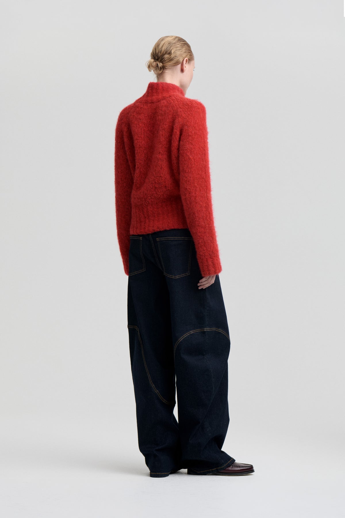 Model viewed from behind wearing a fuzzy red high-neck sweater and dark wide-leg jeans with contrast stitching.
