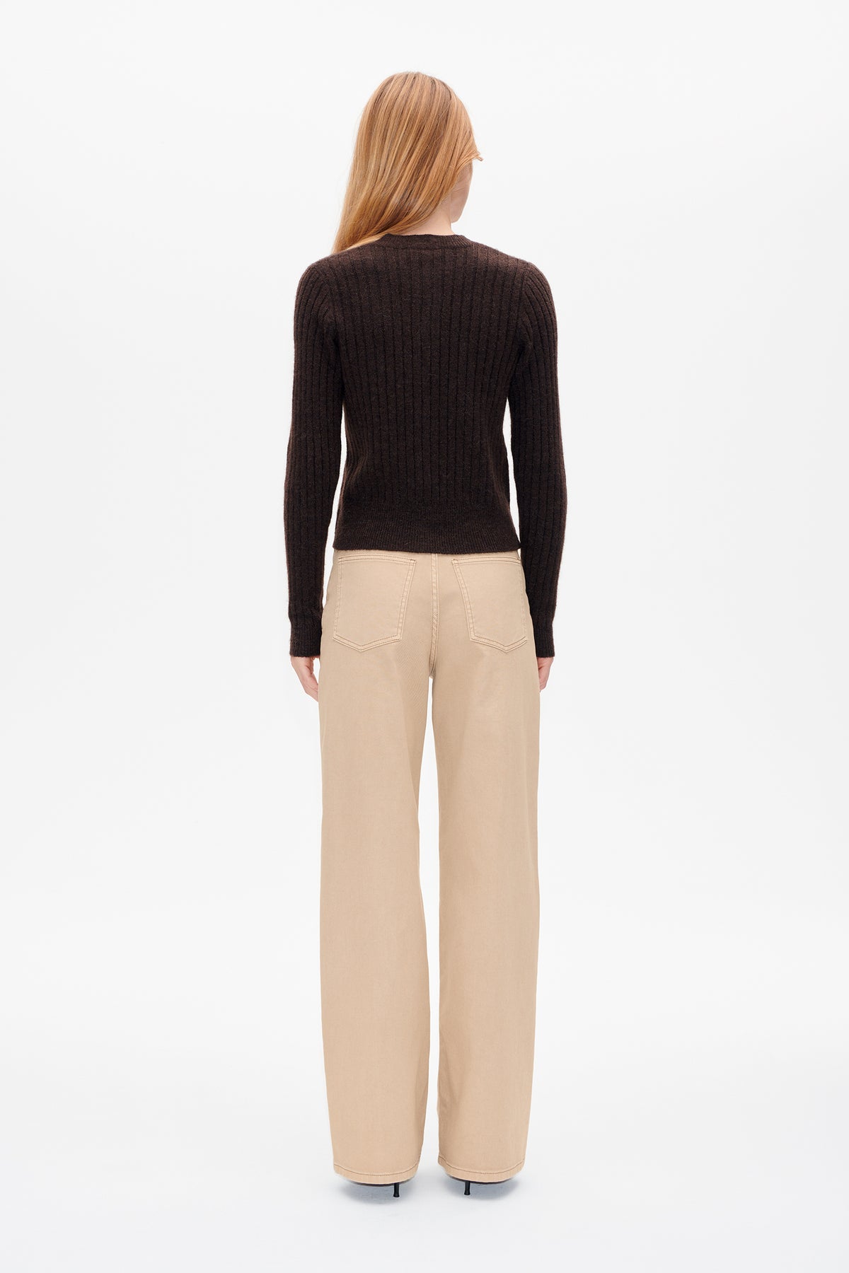 Back view of a model wearing a dark brown ribbed long-sleeve sweater and beige wide-leg trousers.