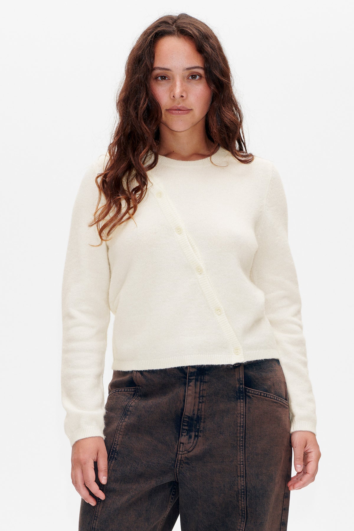 Front view of a model wearing an ivory knit cardigan with a round neckline, long sleeves and button fastening.