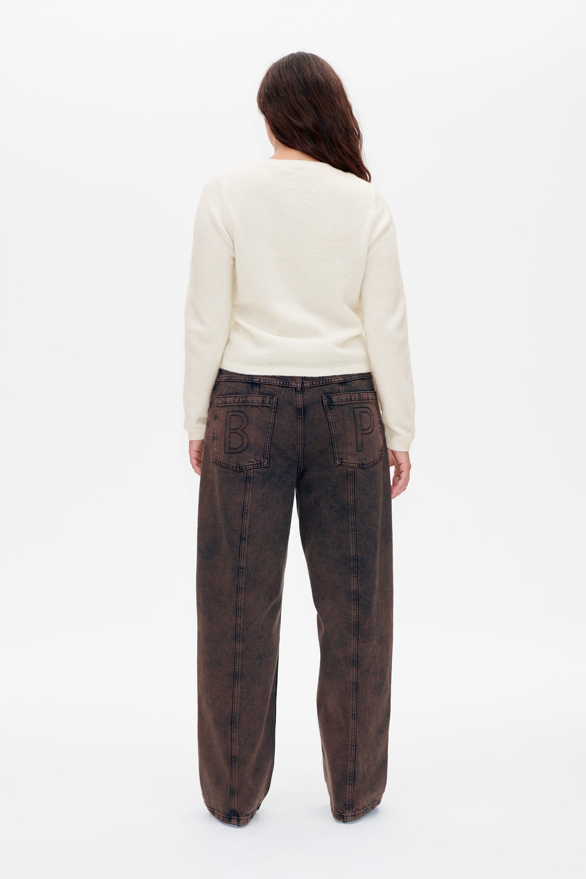 Rear view of a model wearing an ivory knit sweater and wide-leg washed brown jeans with outlined lettering on the back pockets.