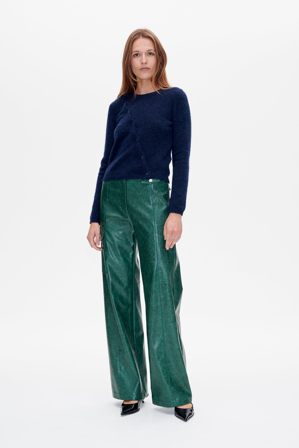 Front view of a model wearing a navy button-front knit cardigan with wide-leg green trousers in a glossy, mottled finish.
