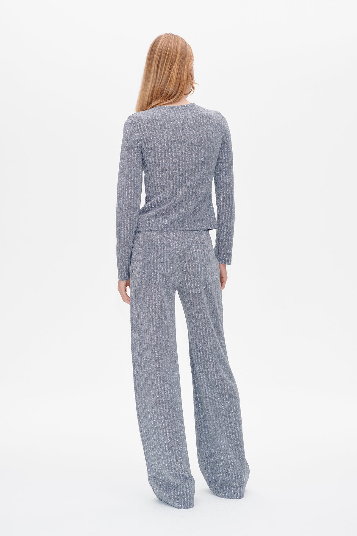 Back view of a model wearing a grey ribbed long-sleeve top and matching wide-leg trousers with subtle shimmer.