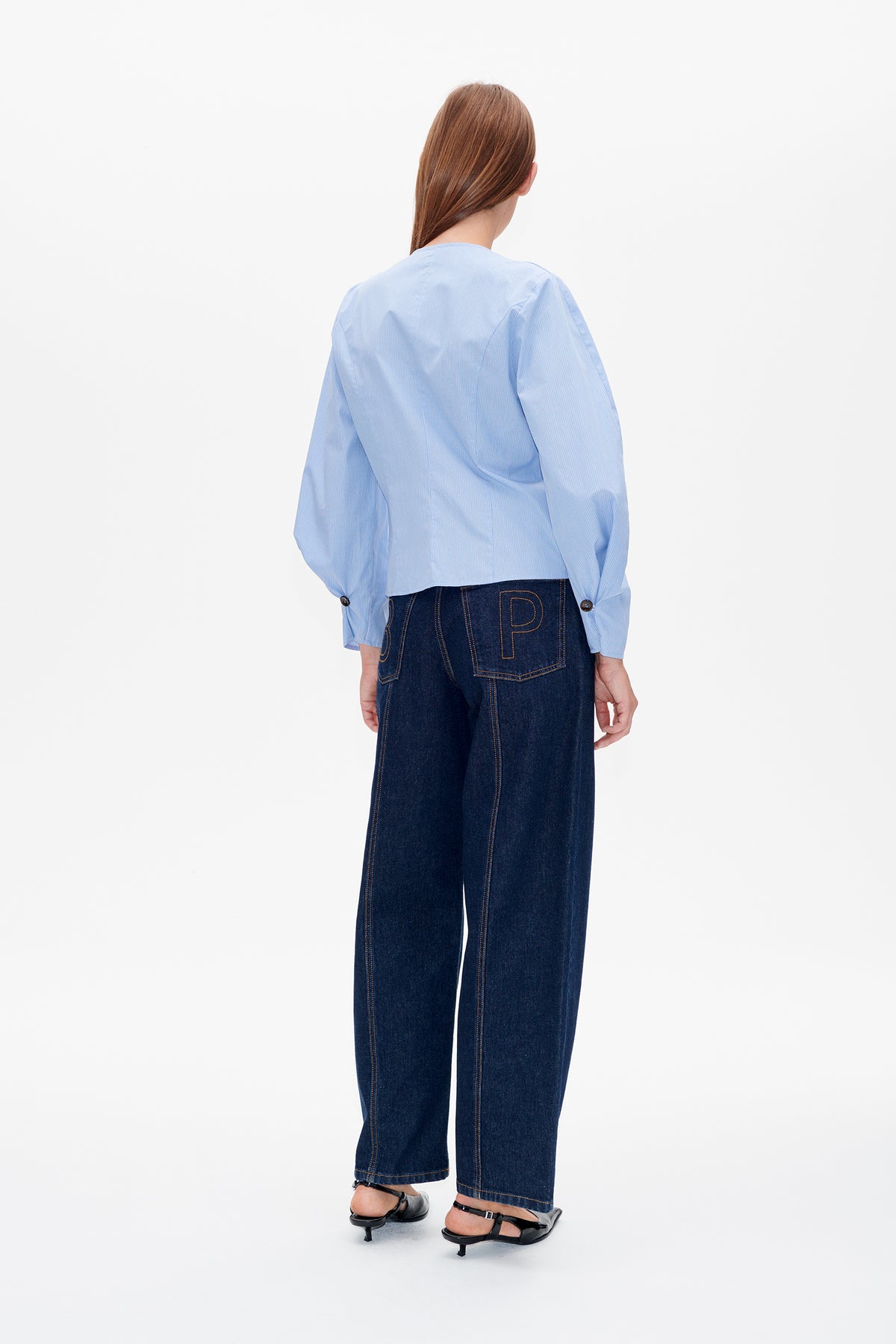 Rückansicht einer hellblauen Bluse mit feinen Nadelstreifen und voluminösen Ärmeln, kombiniert mit dunklen, weit geschnittenen Jeans mit konturierten Gesäßtaschen.