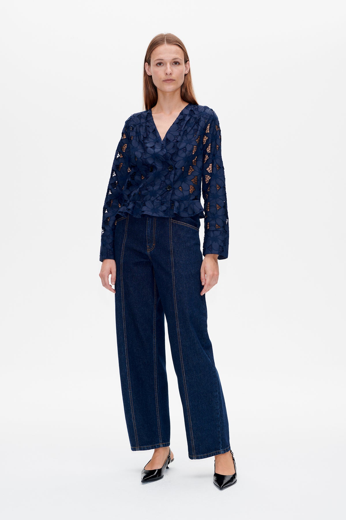 Front view of a model wearing a navy floral cutwork jacket with a V-neck and double-breasted buttons, paired with dark wide-leg jeans.