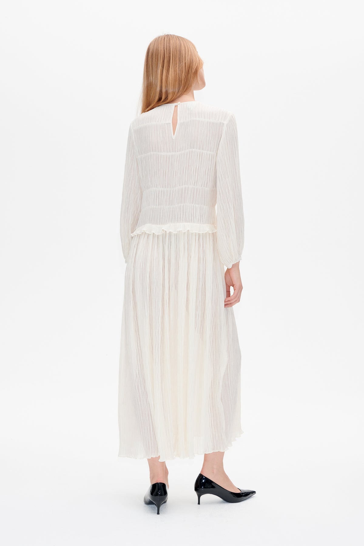 Back view of a sheer white long-sleeved midi dress with a vertical crinkle texture, back keyhole opening and ruffled waist seam.
