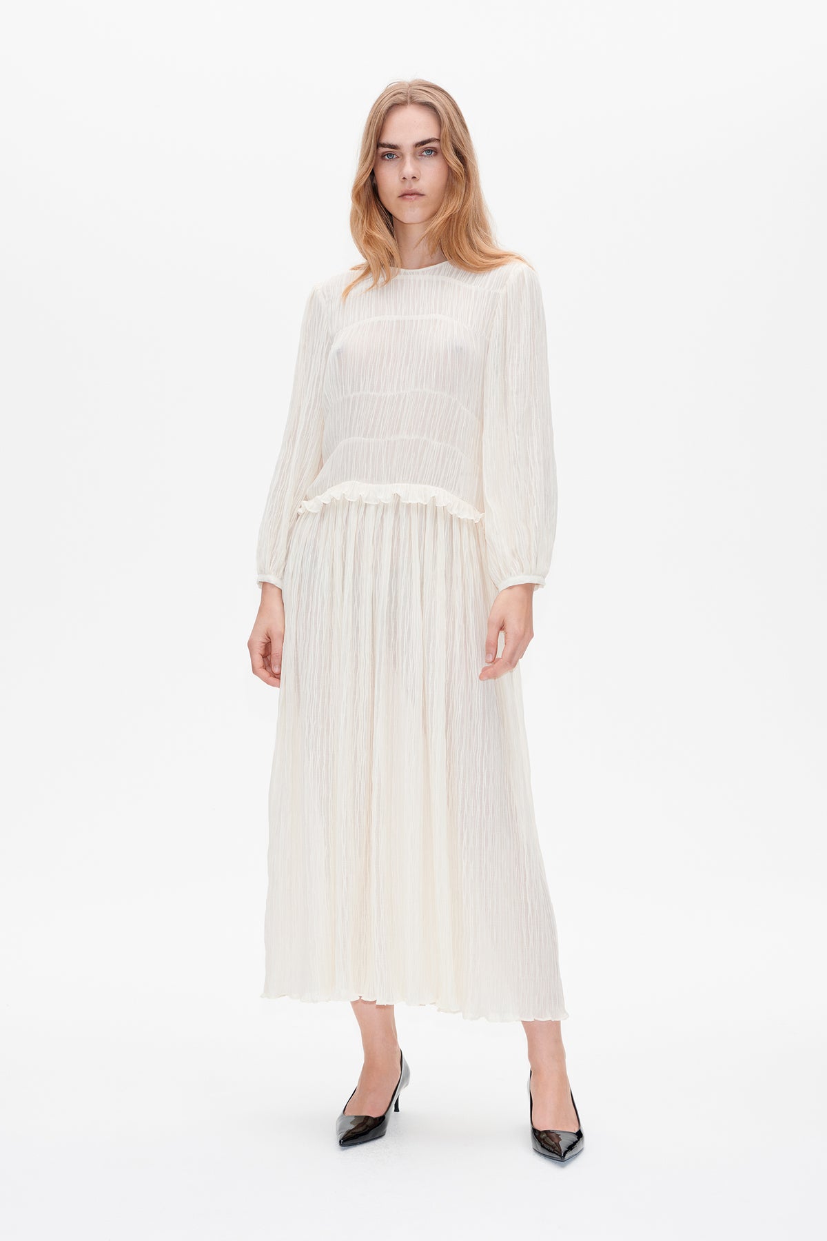 Front view of a long ivory dress with sheer textured stripes, long sleeves, and a ruffled waist seam.
