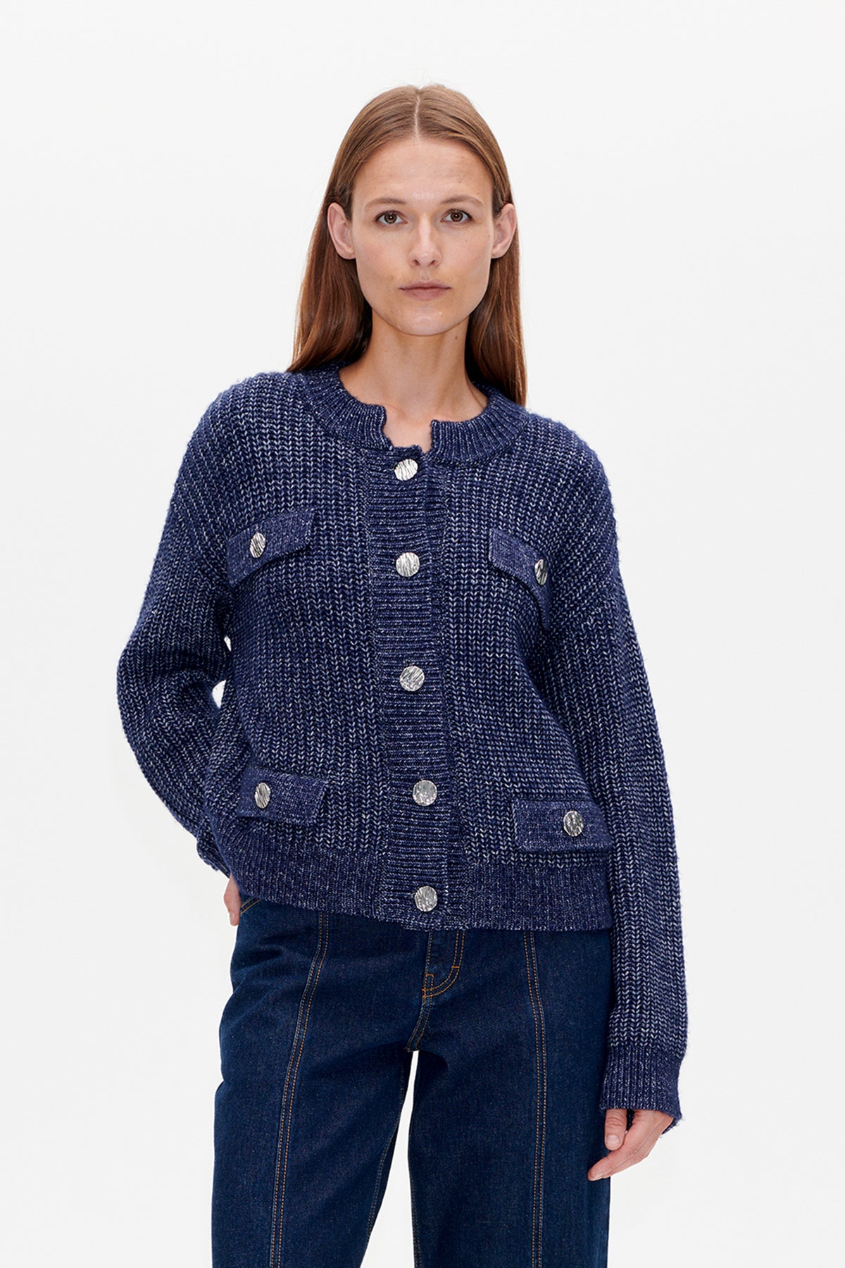 Front view of a model wearing a navy-and-white textured knit cardigan with silver buttons and darker blue patch pockets.