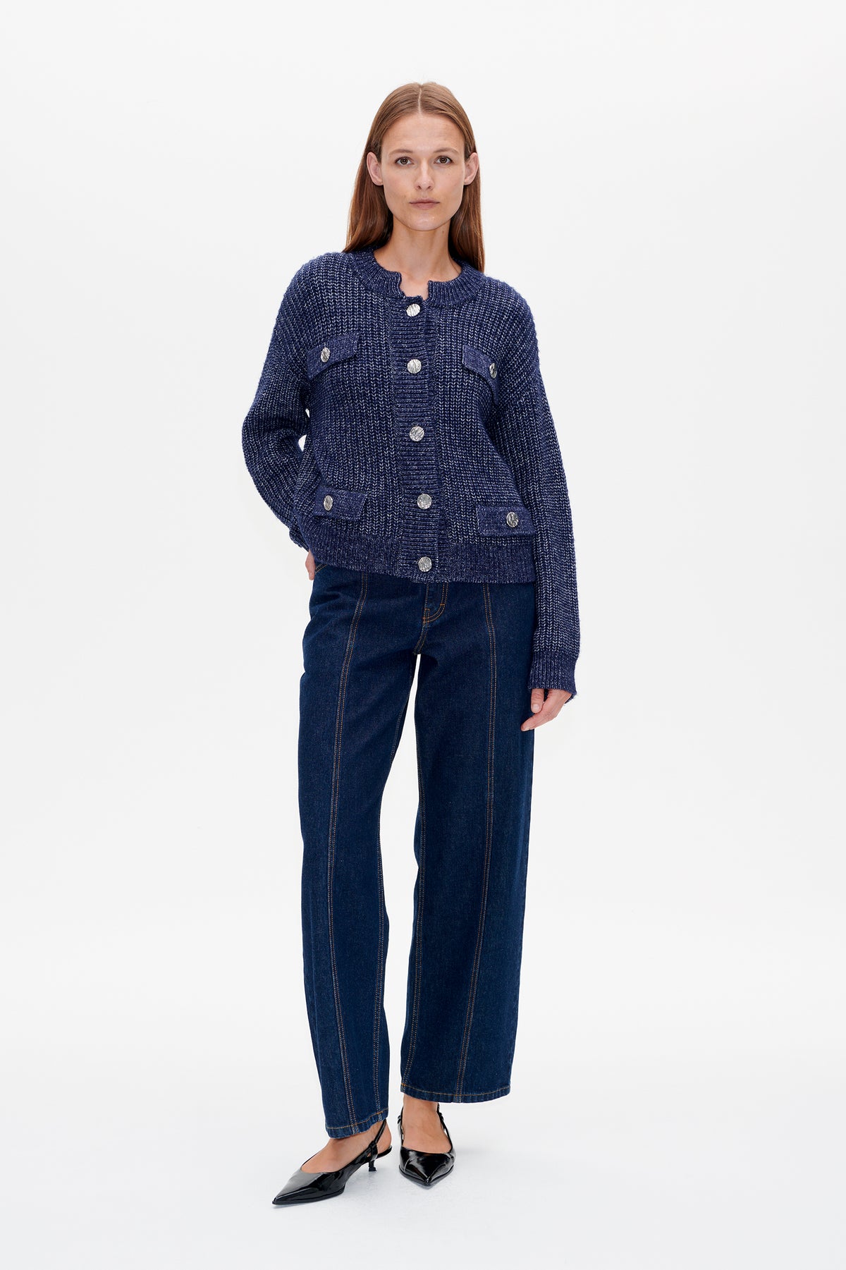 Front view of a model wearing a navy textured knit cardigan with silver buttons and flap pockets, paired with dark jeans.