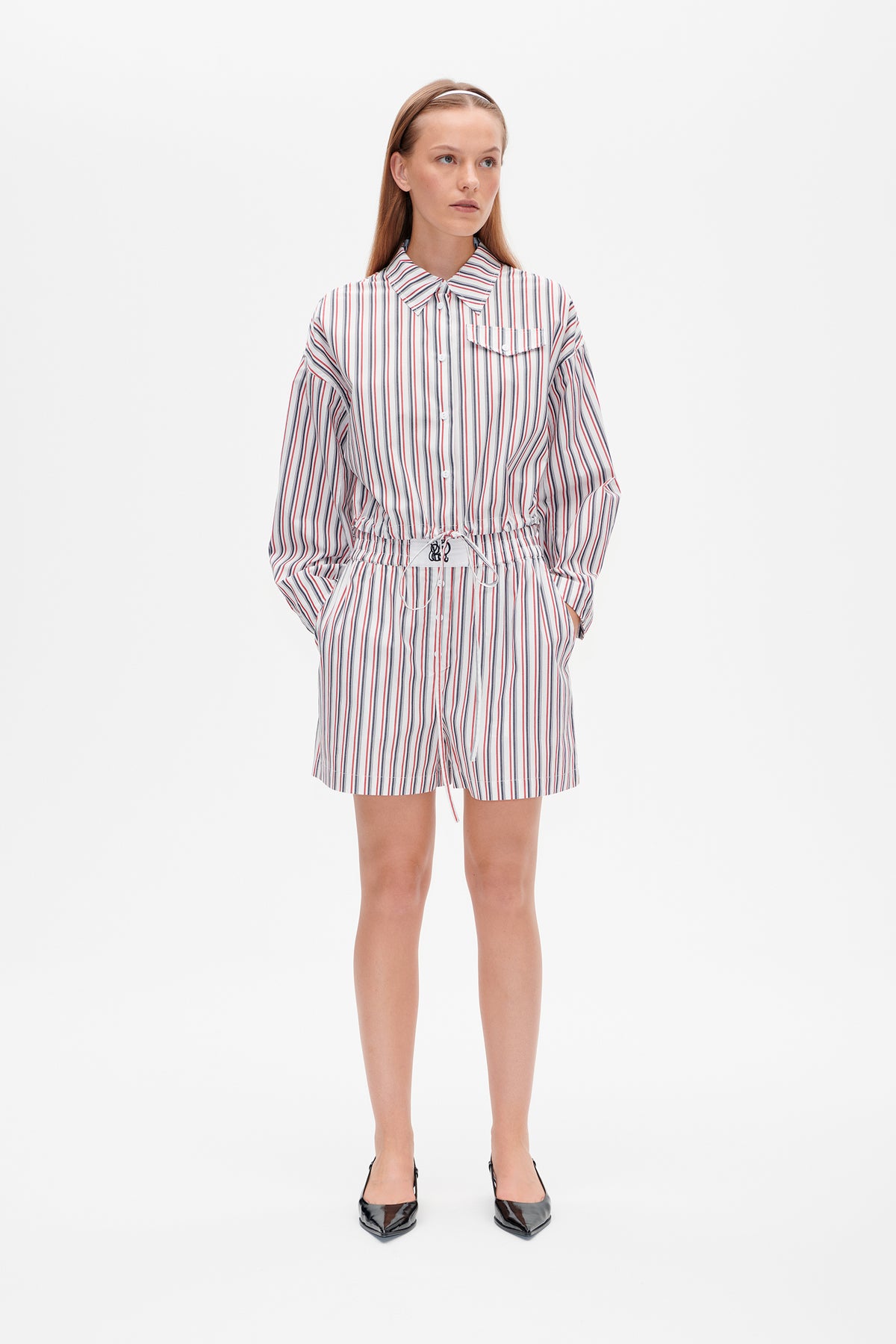 Model wearing a white striped button-front shirt with a chest pocket and drawstring waist, paired with matching shorts.