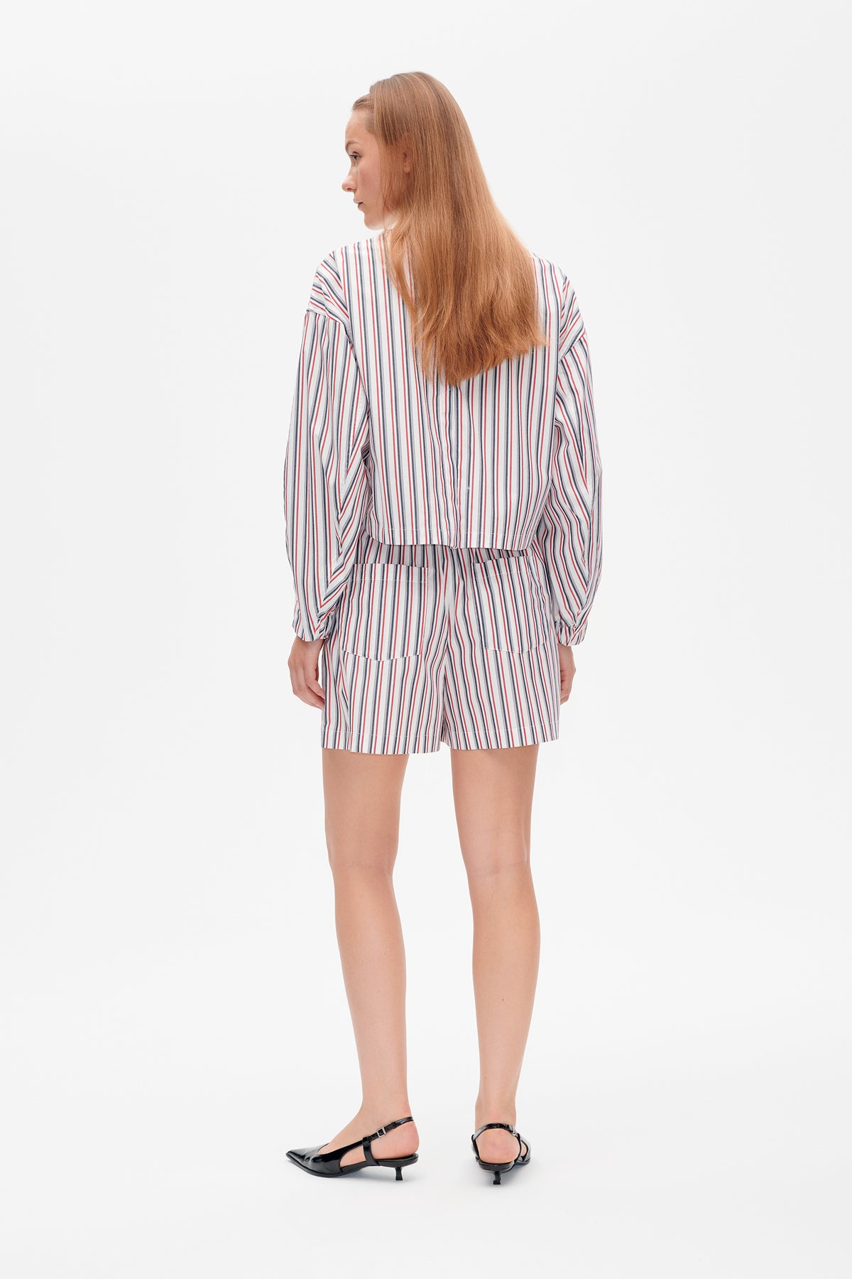 Rear view of a model wearing a white long-sleeved top and shorts with red, navy and grey vertical stripes.