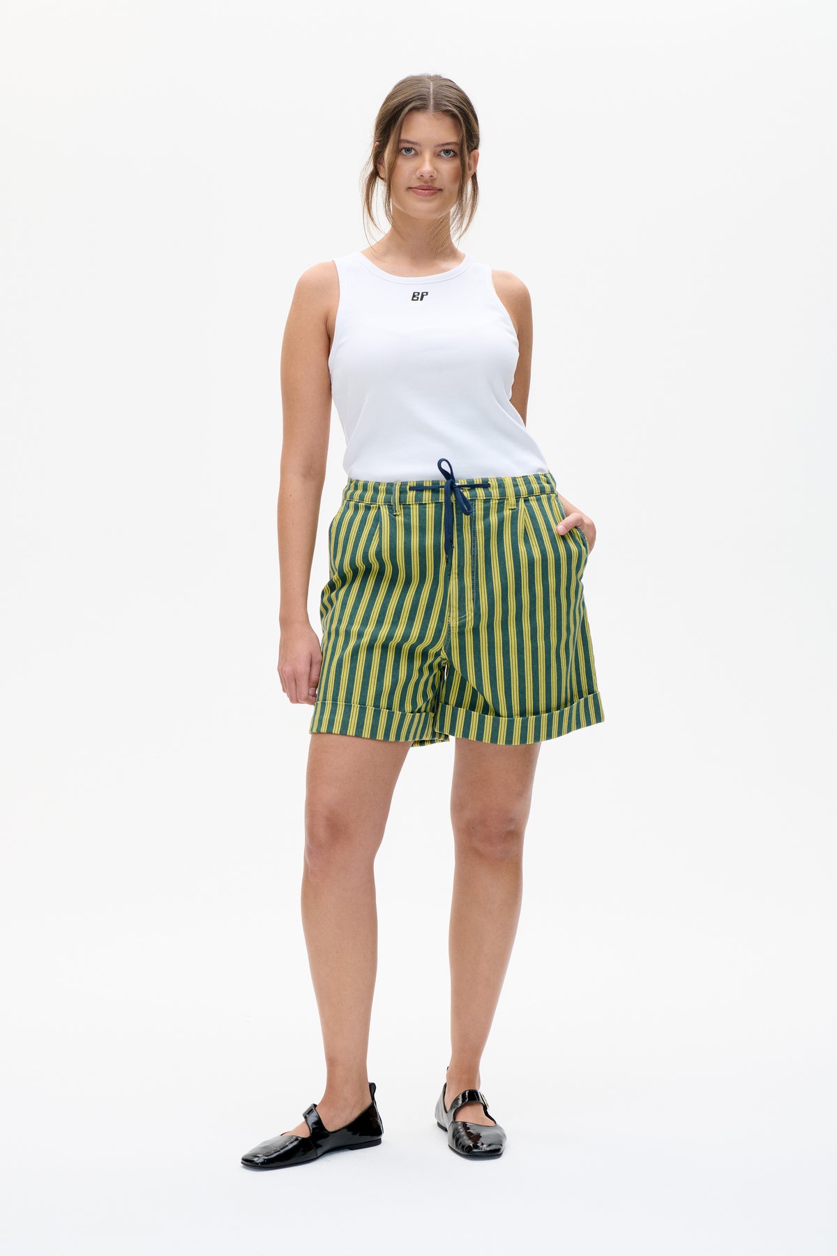 Vue de face d'un top sans manches blanc avec un petit logo sur la poitrine, porté avec un short rayé vert et jaune.