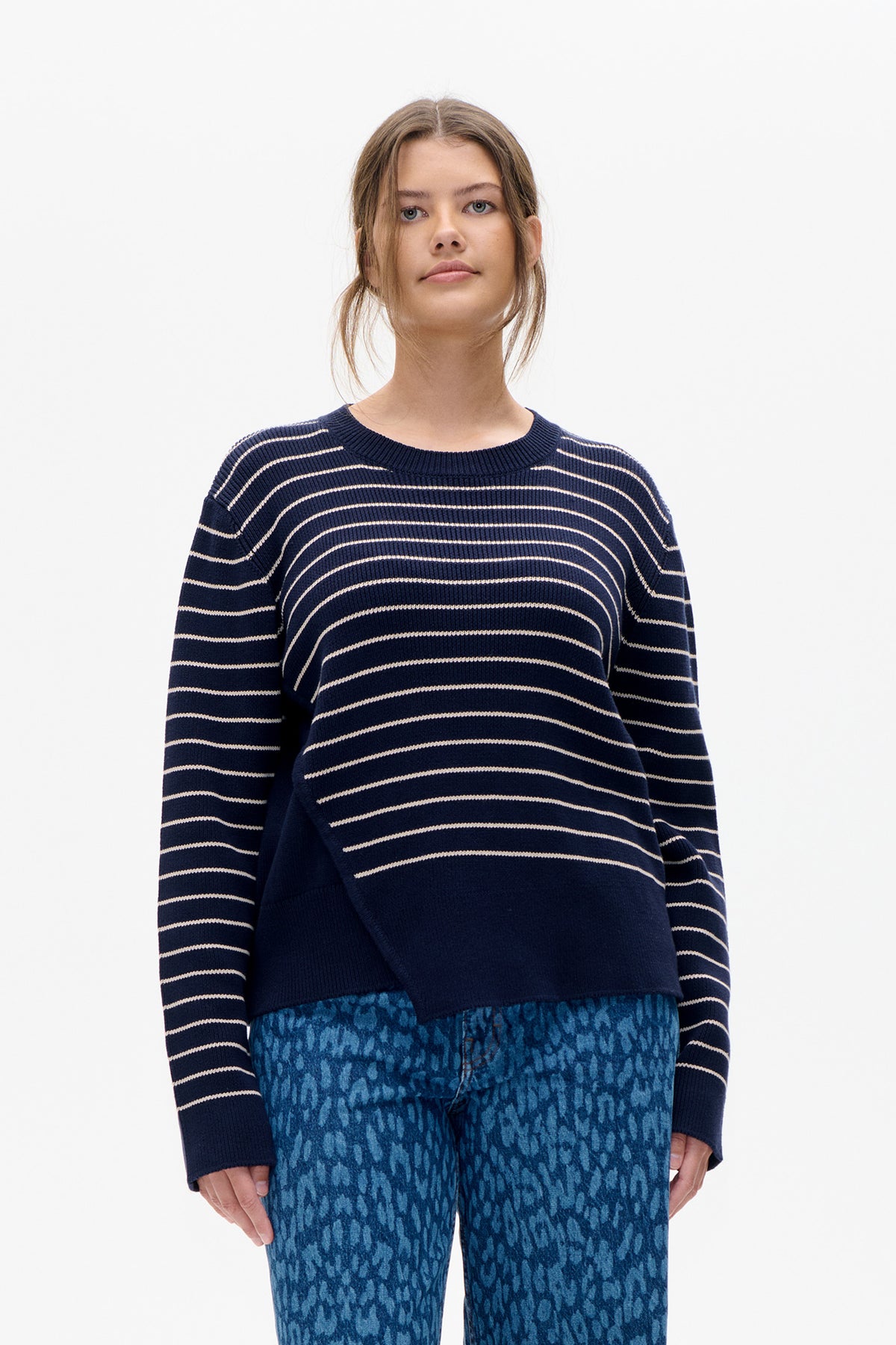 Front view of a navy rib-knit crewneck sweater with thin cream horizontal stripes, worn with blue patterned trousers.