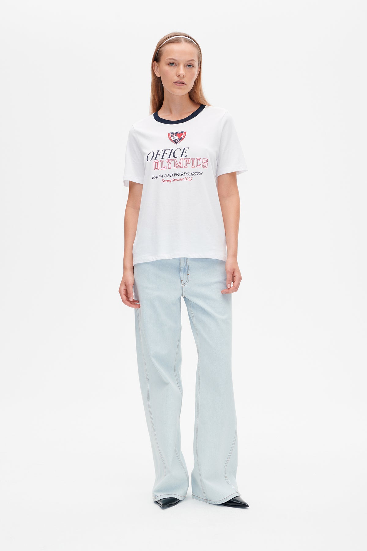Model wearing a white short-sleeved T-shirt with a navy neckline and red-and-navy chest lettering, paired with pale blue flared jeans.
