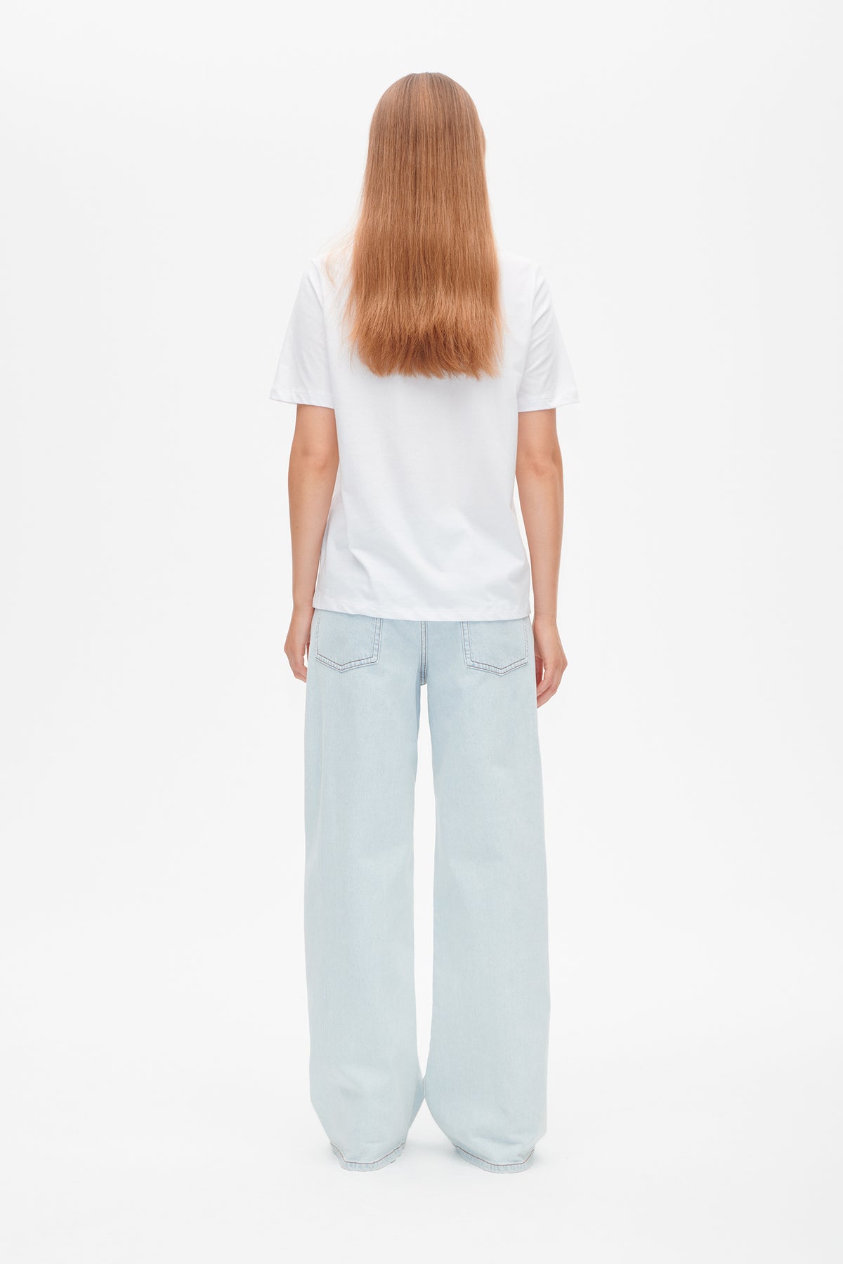 Back view of a plain white short-sleeve T-shirt, styled with pale blue wide-leg jeans.