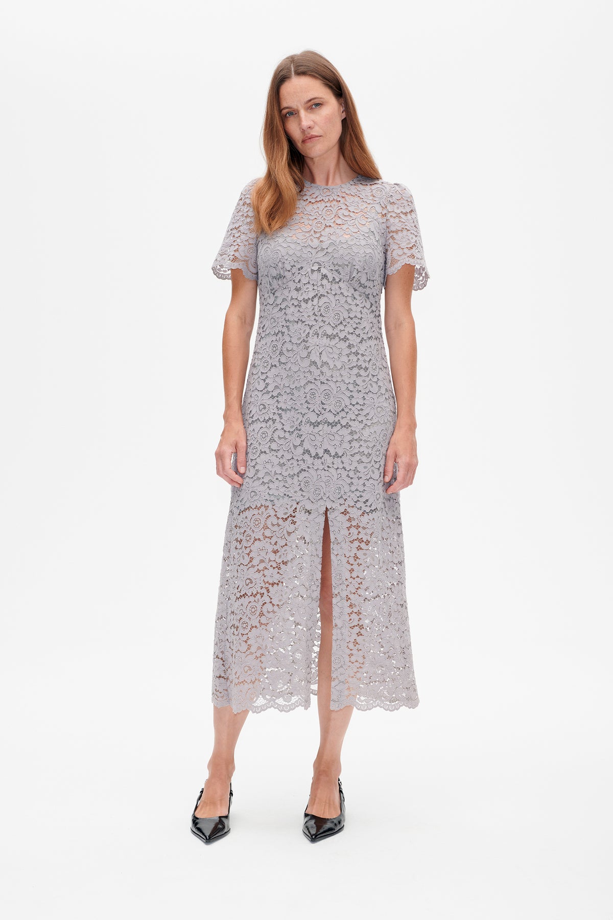 Front view of a model wearing a light grey floral lace midi dress with short sleeves, scalloped edges and a front slit.