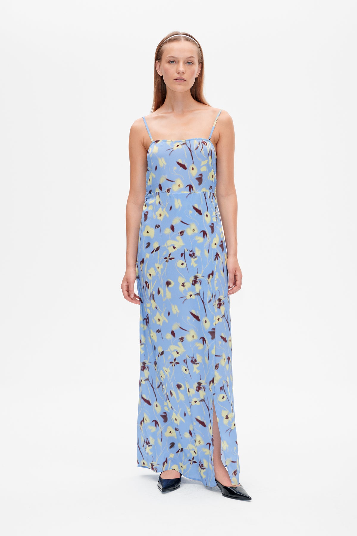 Front view of a light blue spaghetti-strap maxi dress with an abstract yellow and burgundy floral print and front slit.