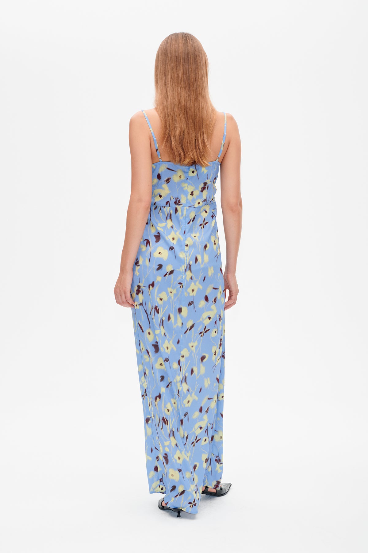 Achteraanzicht van een lange blauwe jurk met spaghettibandjes en een gele en bordeauxrode bloemenprint.