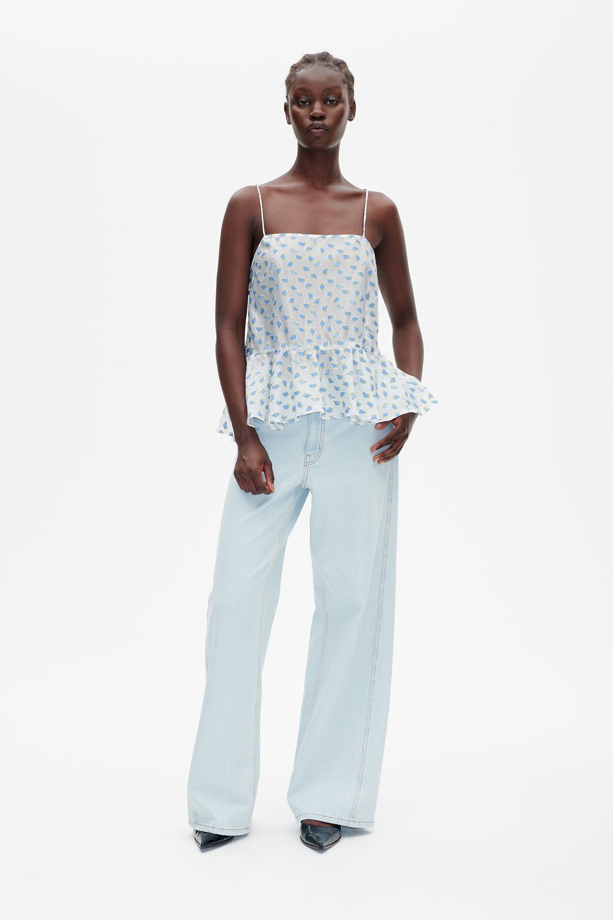 Model wearing a white spaghetti-strap peplum top with small blue and green floral print, paired with light-wash wide-leg jeans.