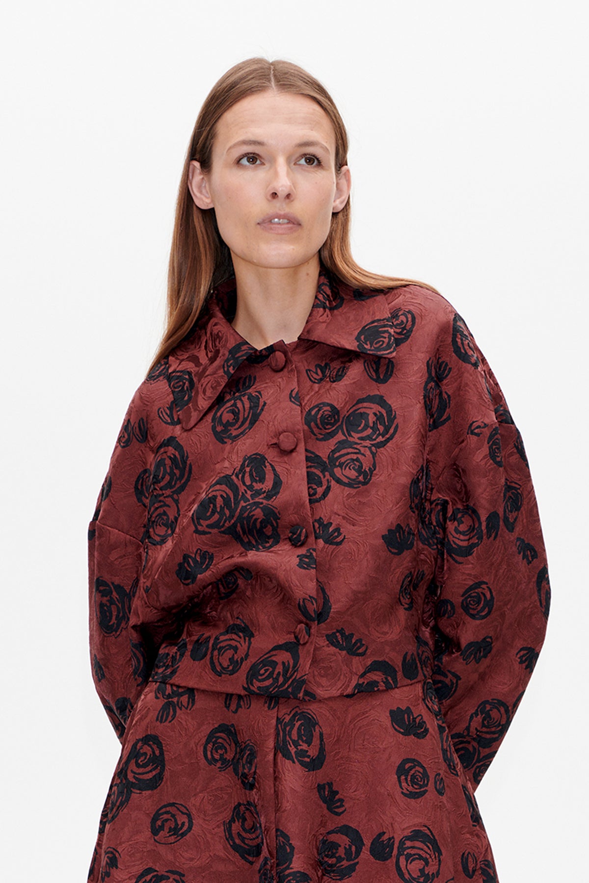 Detailopname van de voorkant van een roestkleurige blouse met zwarte abstracte bloemenprint, bedekte knopen en een brede omgeslagen kraag