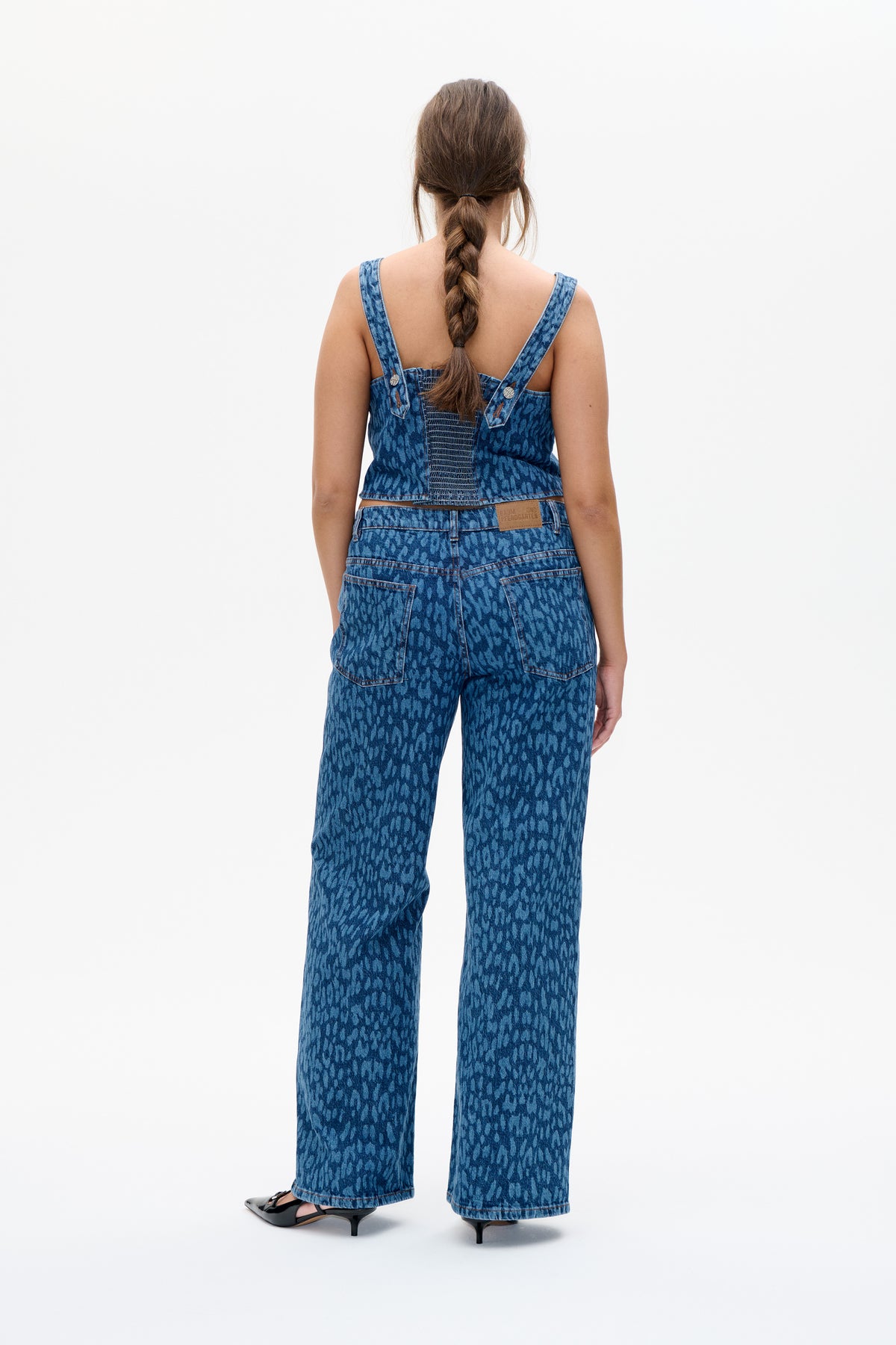 Back view of blue patterned denim overalls with shoulder straps, a smocked bib panel, back pockets and wide legs.