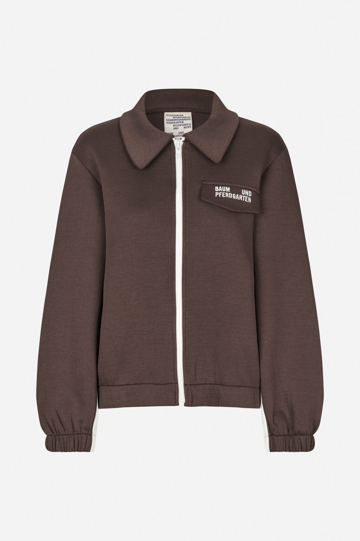 Front view of a dark brown zip-front jacket with a large pointed collar, white zipper, chest logo patch and gathered cuffs.