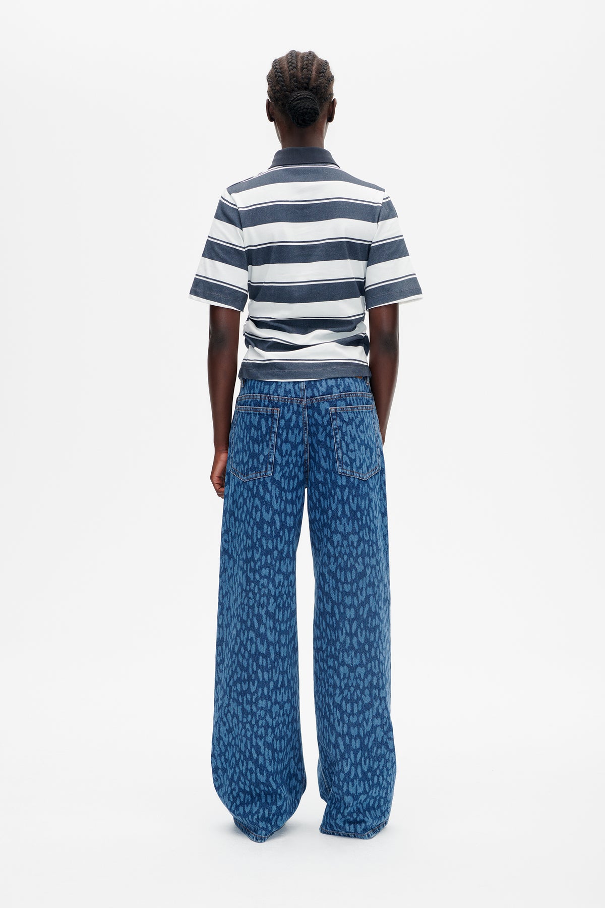Vue de dos d'un mannequin portant une chemise à col et manches courtes, rayée bleu marine et blanc, et un jean large bleu à motif.