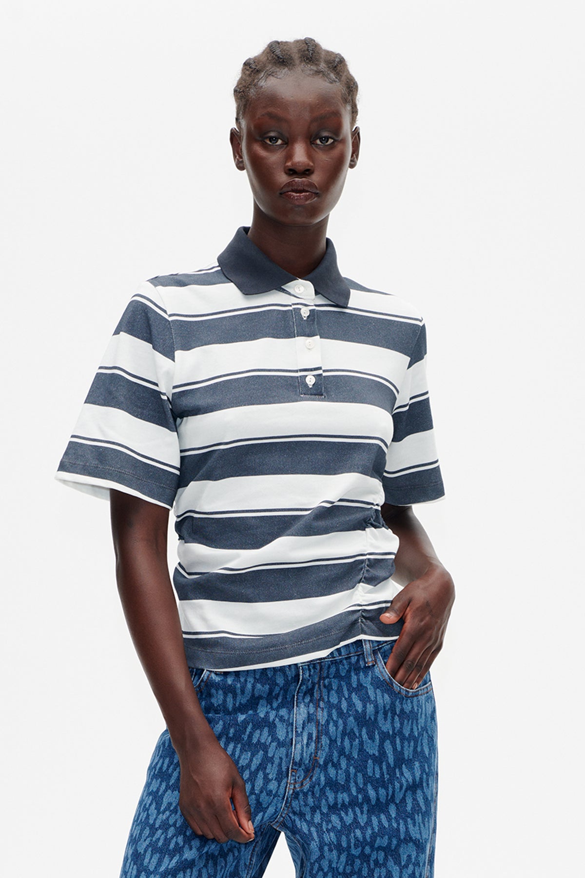 Front-facing model wearing a navy and white striped short-sleeve polo with a dark collar and blue patterned jeans.