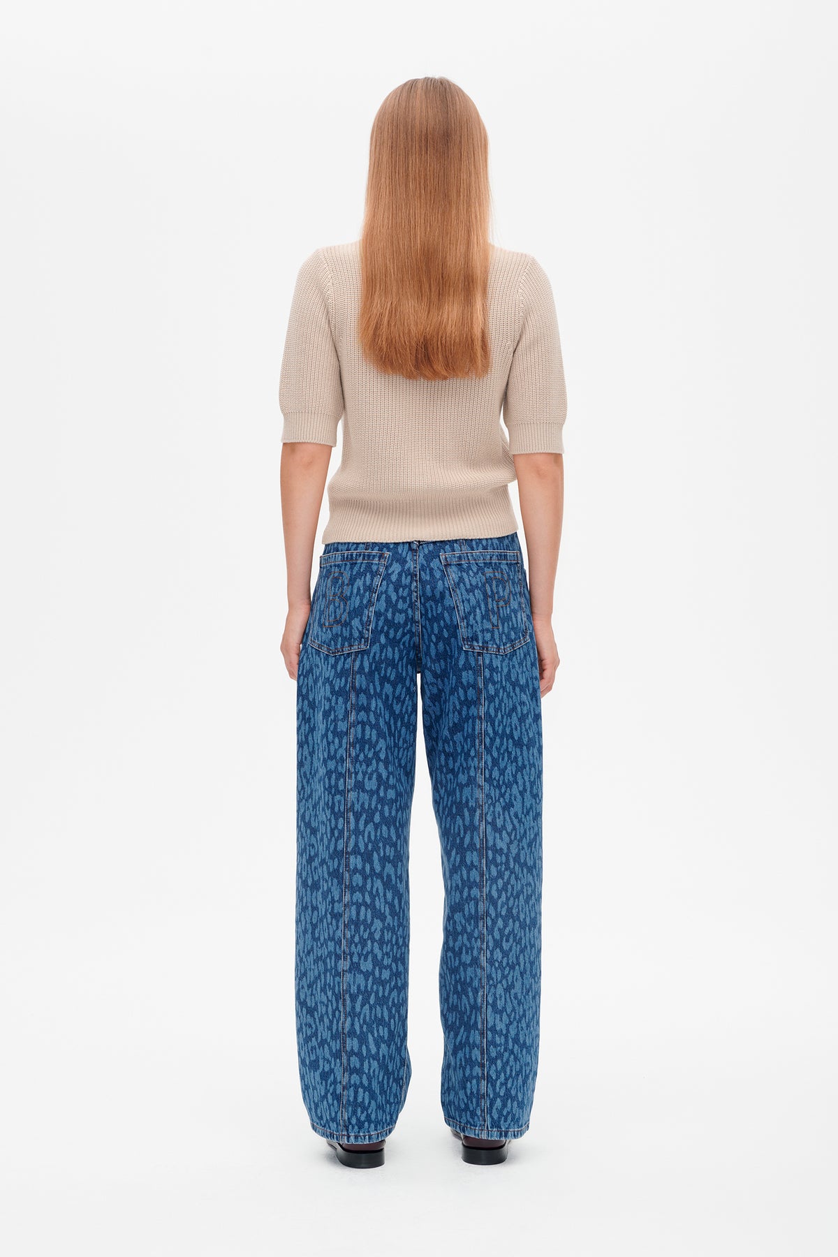 Back view of a model wearing a beige short-sleeve knit top and blue wide-leg jeans with an all-over pattern and back pockets.