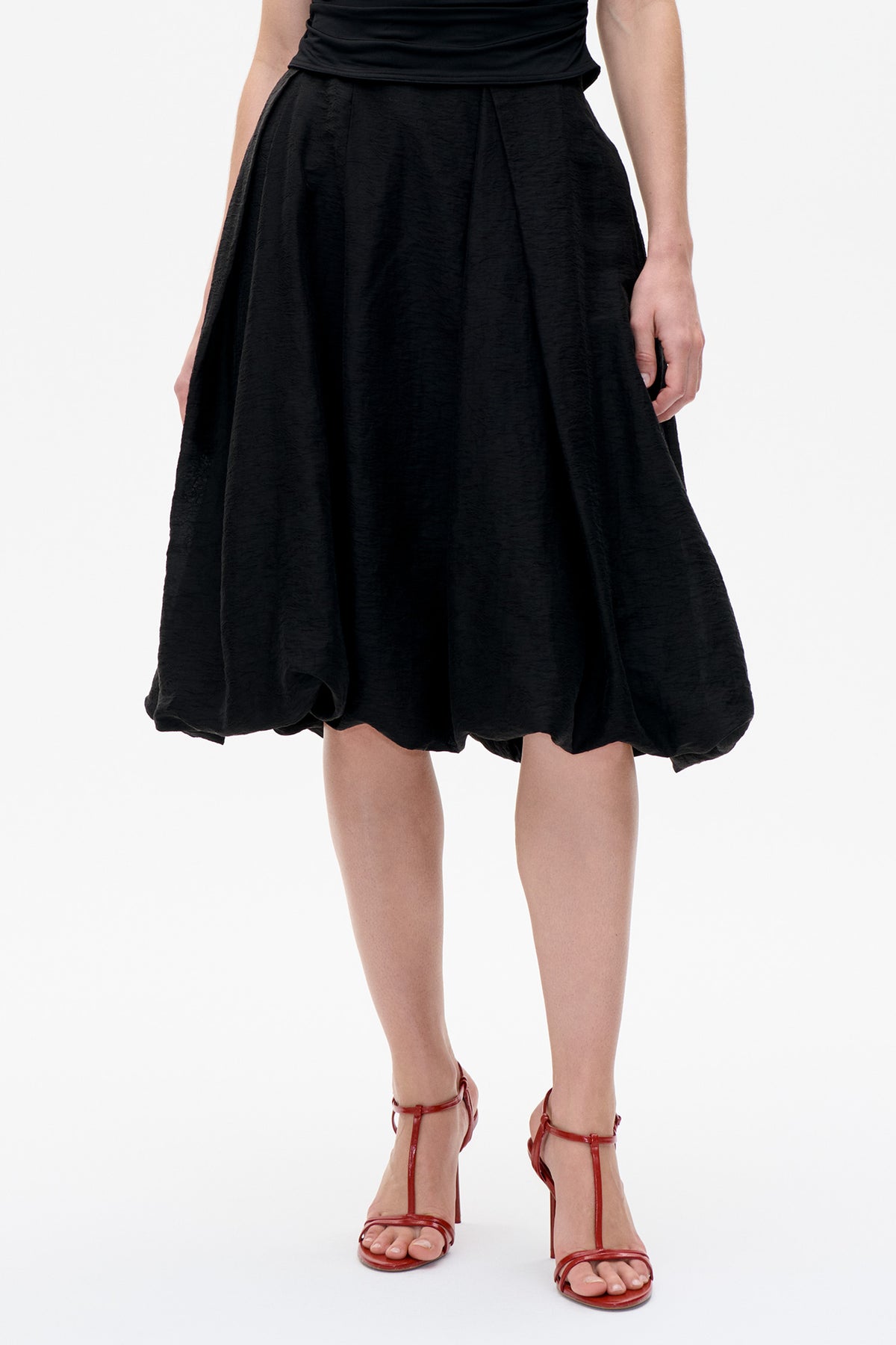 Close-up front view of a black voluminous skirt with soft pleats and a rounded, gathered hem