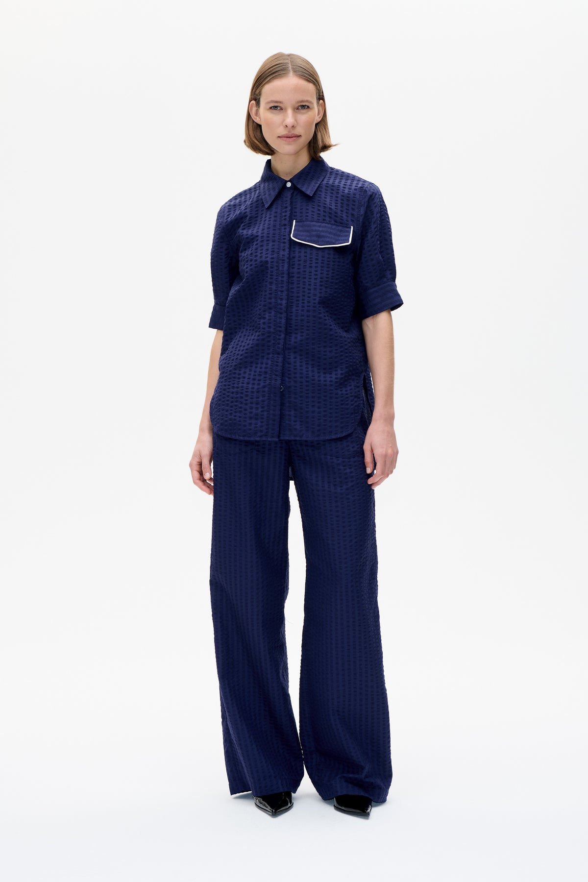 Vue de face d'un mannequin portant une chemise texturée bleu marine à manches courtes avec une poche bordée de blanc et un pantalon à larges jambes assorti.