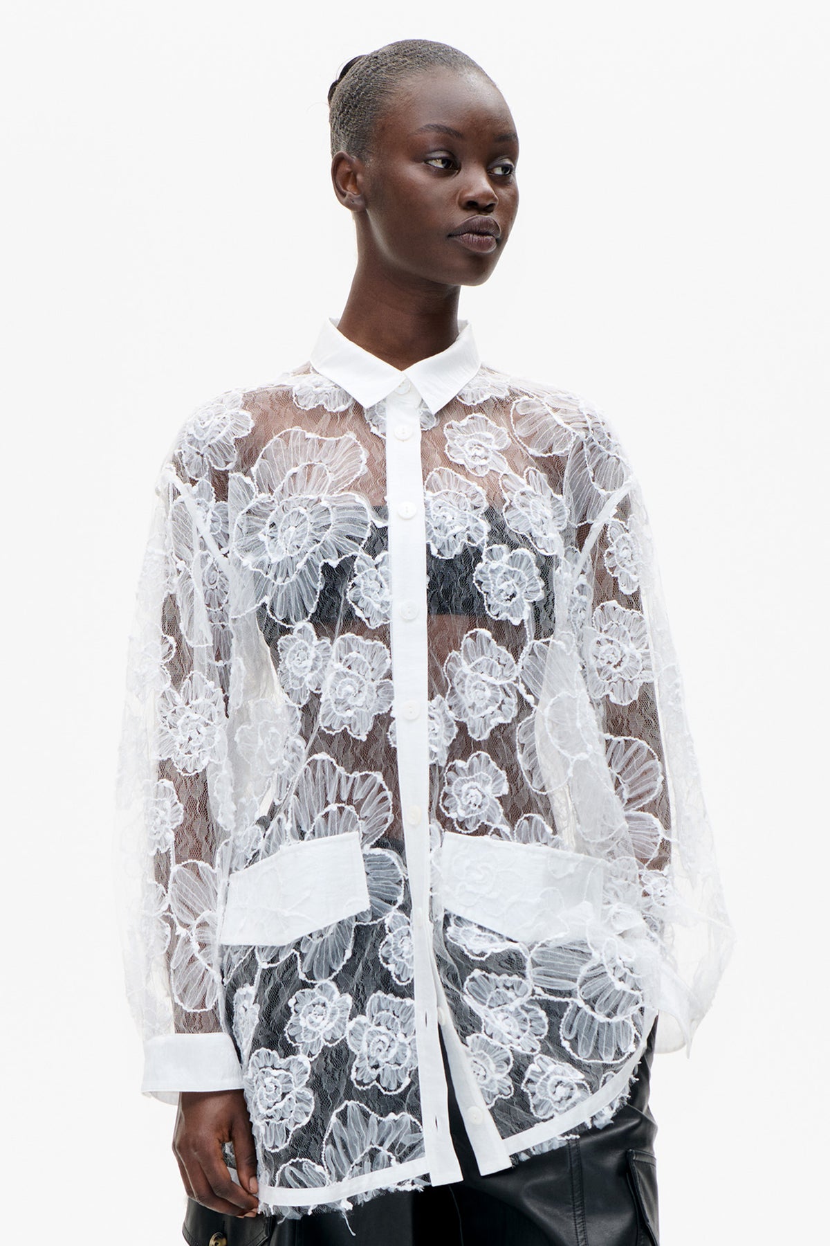 Front close-up of a sheer white blouse with raised floral lace, a pointed collar, button placket and wide cuffs.