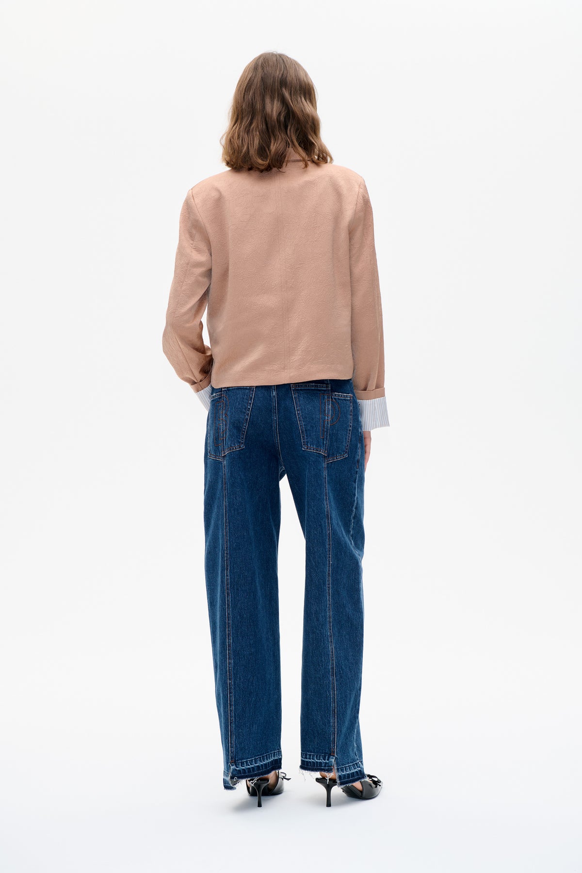 Back view of a model wearing a blush pink long-sleeved top with an embossed crinkled texture and dark blue wide-leg jeans.