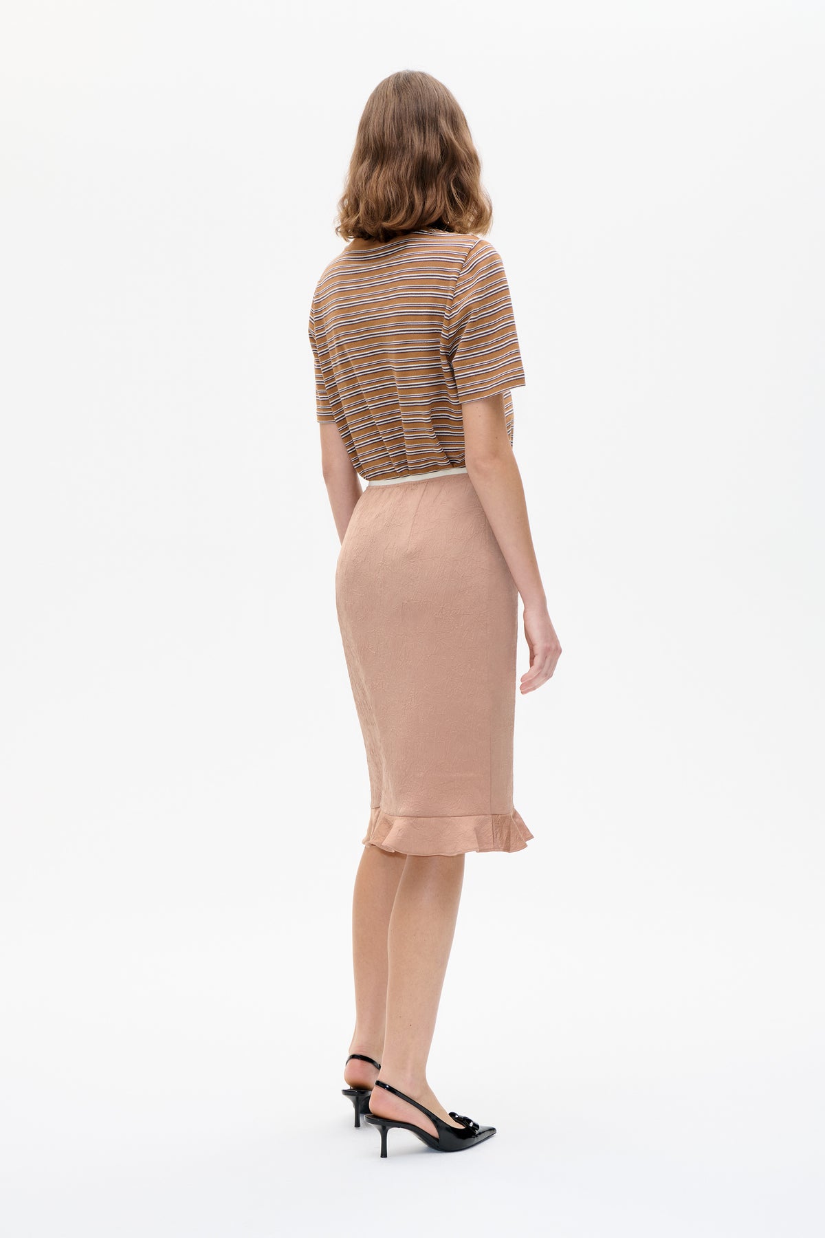 Achteraanzicht van een model met een karamelbruine top met korte mouwen en smalle crème- en donkere strepen, gecombineerd met een lichtroze rok met structuur.