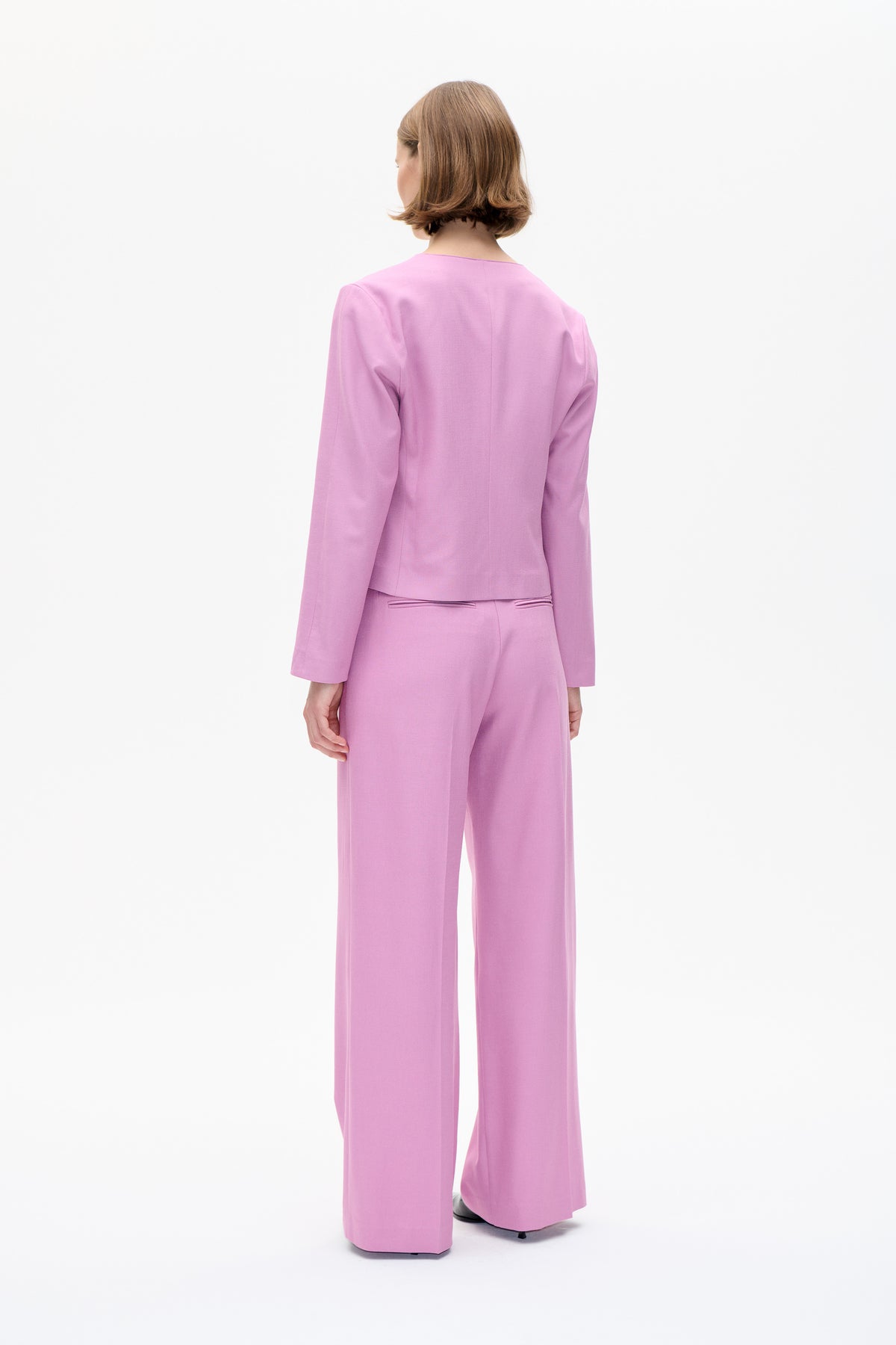 Rear view of a model wearing a solid pink tailored blazer with matching wide-leg trousers.