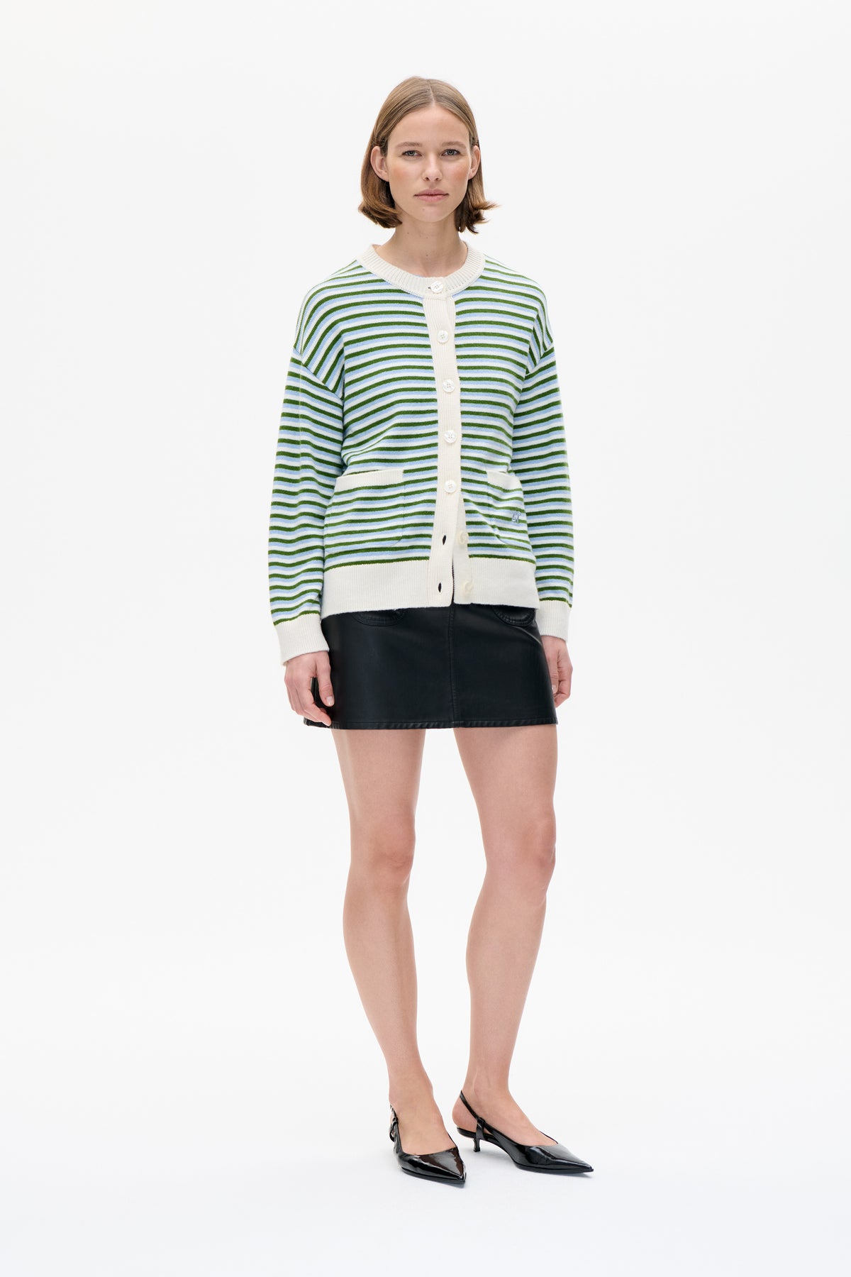 Front view of a model wearing a cream-trimmed cardigan with green and pale blue stripes, paired with a black mini skirt and slingback heels.