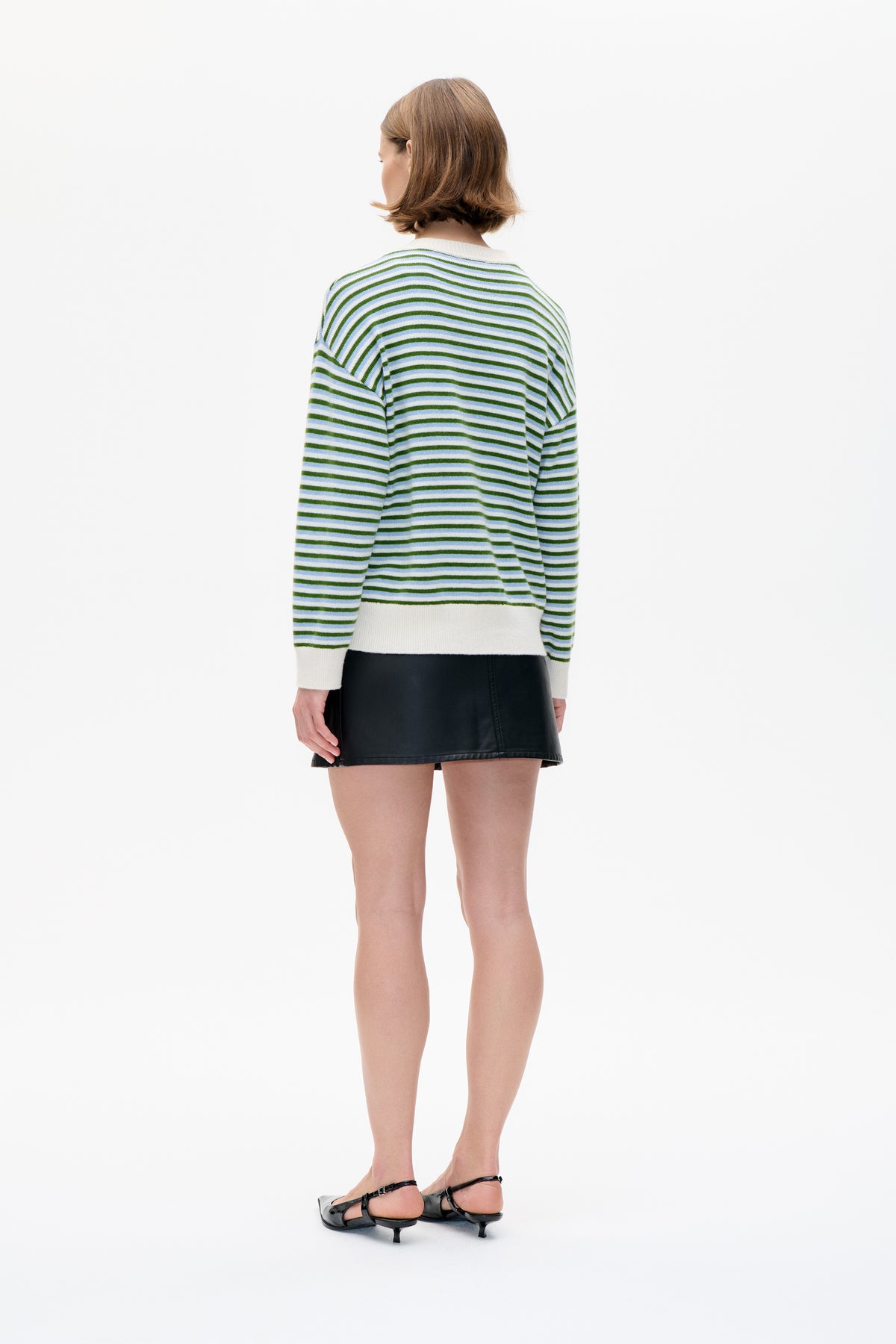 Back view of a model wearing a white knit sweater with green and pale blue horizontal stripes and ribbed cuffs and hem.