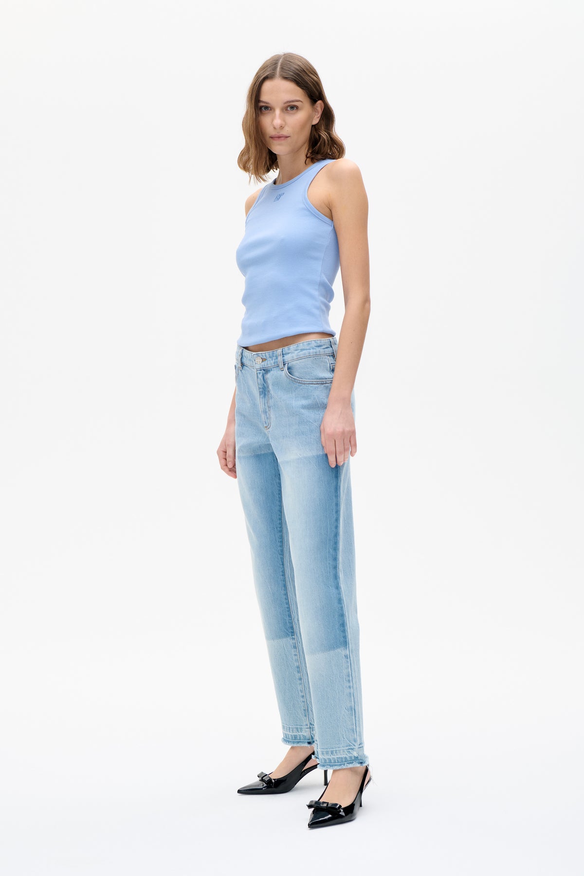 Model trägt ein hellblaues ärmelloses Top mit kleinem Brustlogo, hellgewaschene, verkürzte Jeans und schwarze Pumps mit Schleifendetail