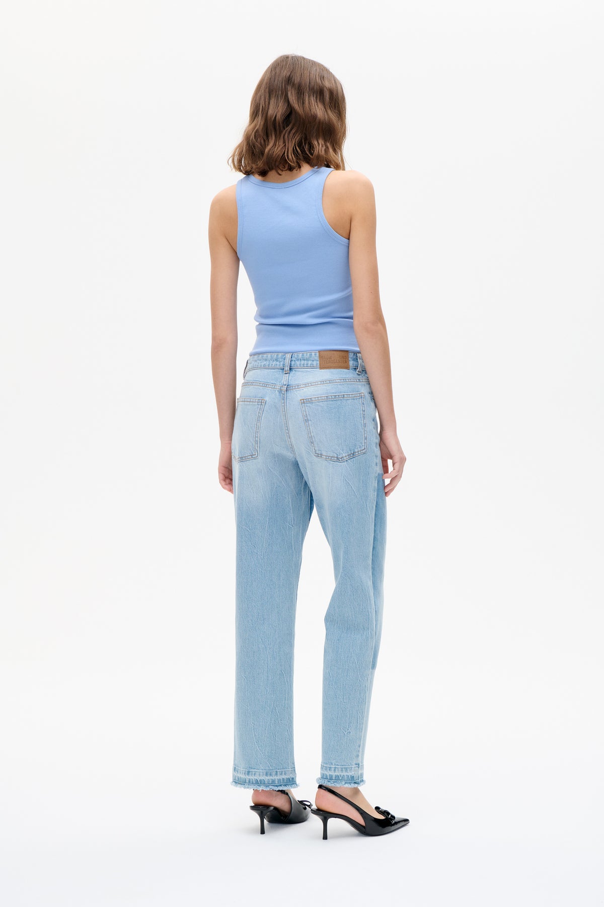 Back view of a model wearing a pale blue sleeveless ribbed tank top, light-wash wide-leg jeans with frayed hems, and black heels.