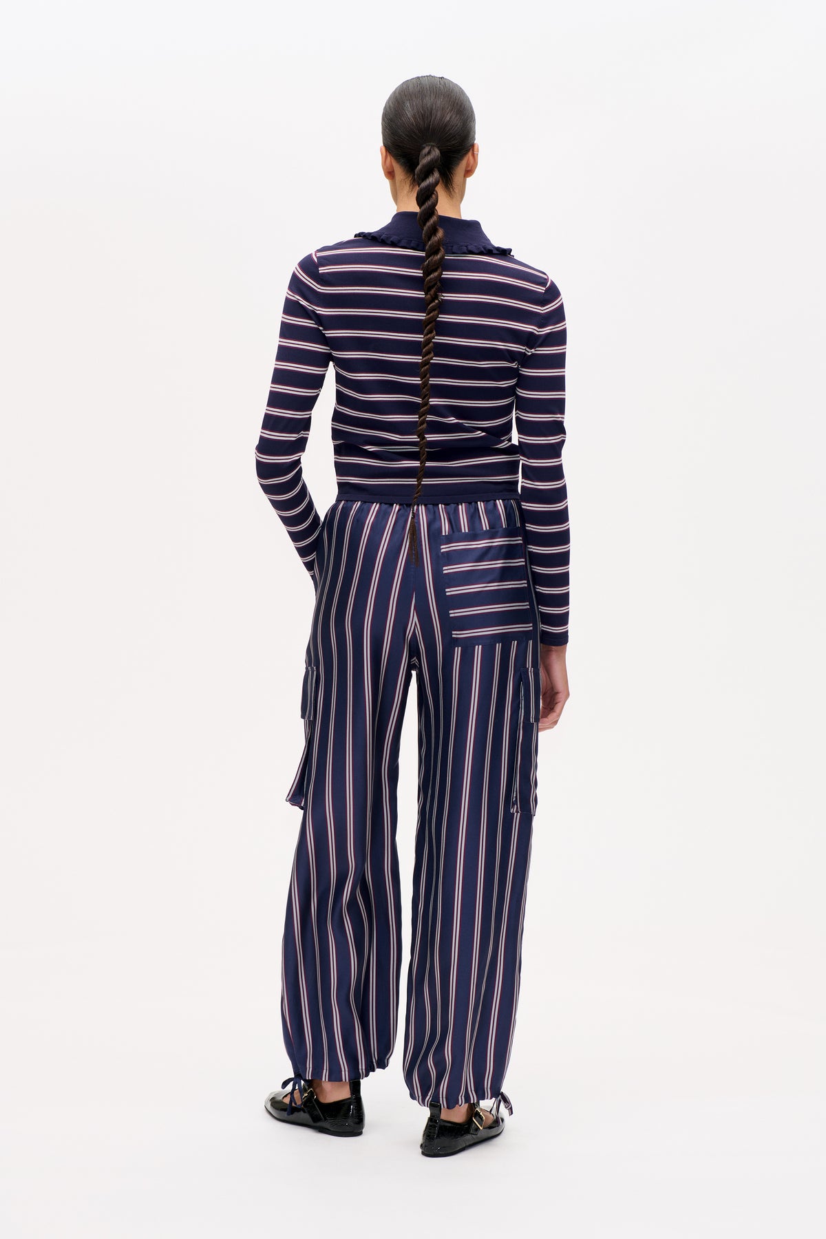 Rückansicht eines Models in einem marineblauen Langarmtop mit Querstreifen und Rüschenkragen, kombiniert mit einer vertikal gestreiften Hose.