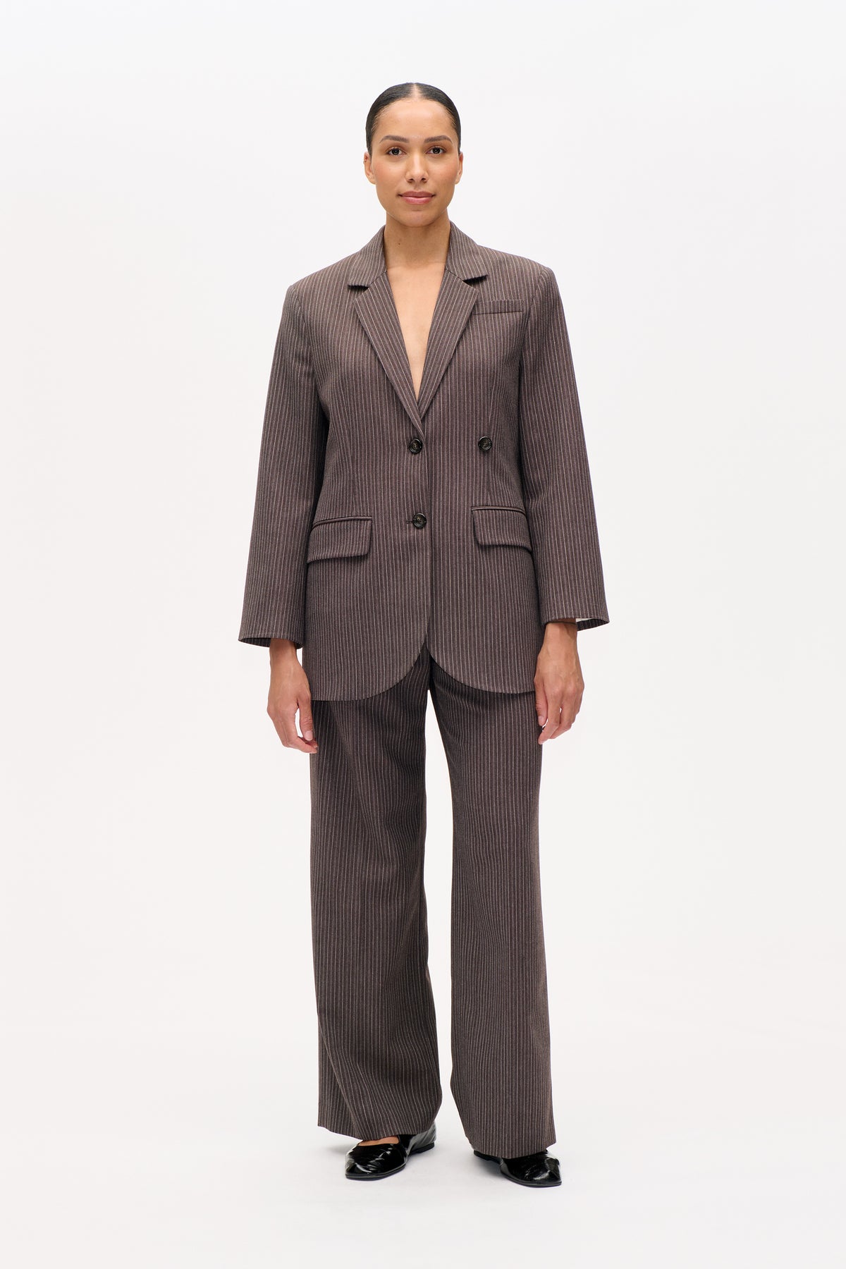 Vooraanzicht van een model in een bruin, fijn krijtgestreept, dubbelgeknoopte blazer met bijpassende broek met wijde pijpen.