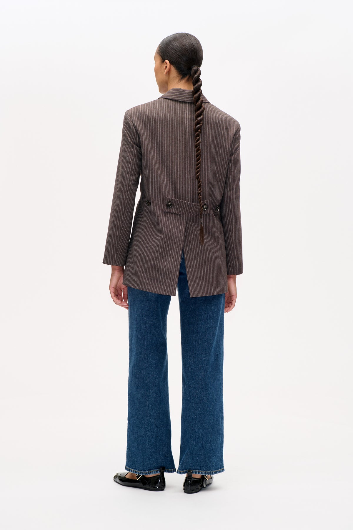 Achteraanzicht van een bruine blazer met krijtstrepen en een tailleband met knoopsluiting, gecombineerd met wijde blauwe jeans.