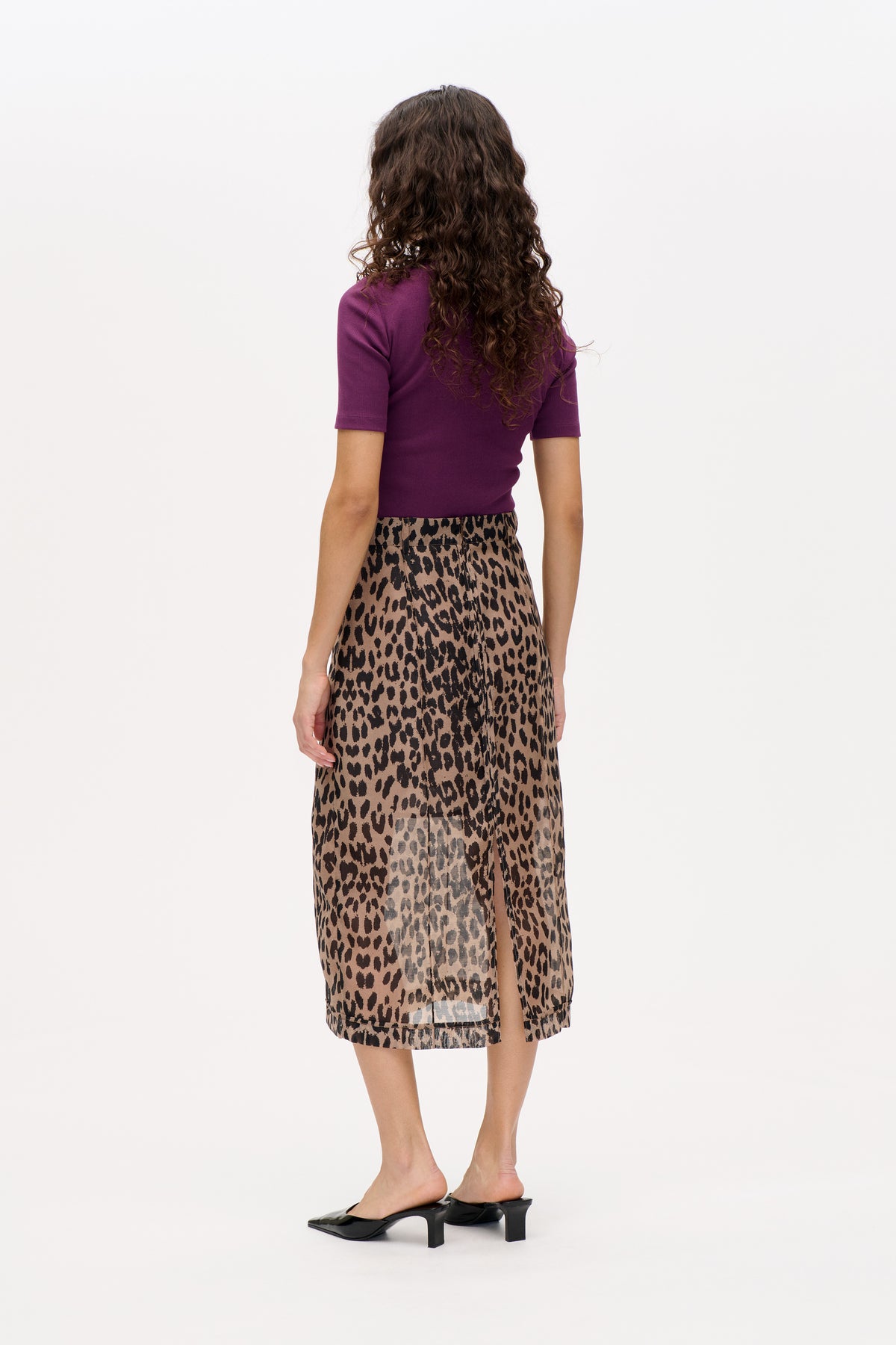 Back view of a model wearing a plum short-sleeve top and a taupe midi skirt with a black animal print and side slit.